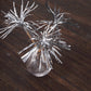Silver firework frills cake toppers in a clear vase on wooden surface.