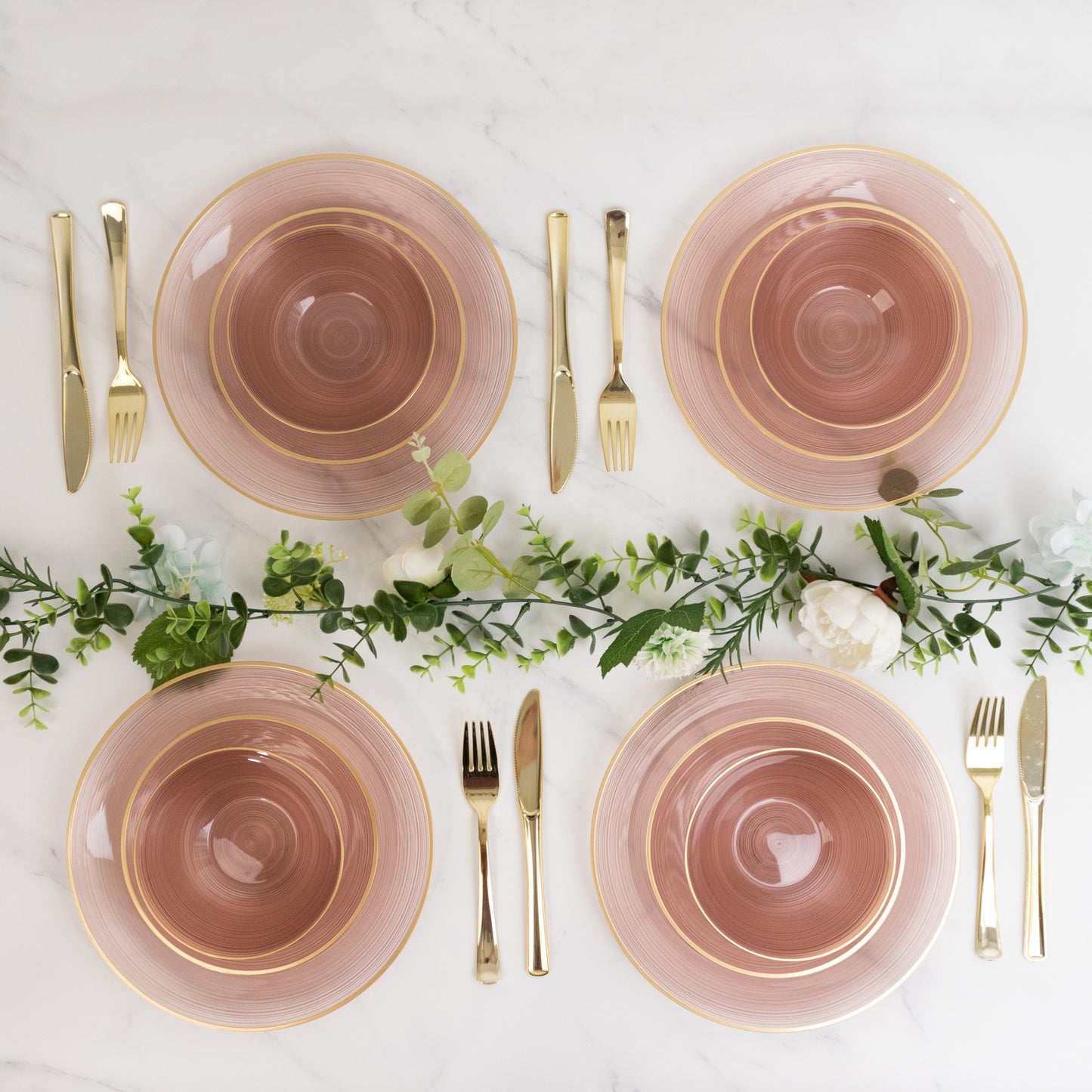 Transparent dusty rose bowls with gold rim on a marble table setting.