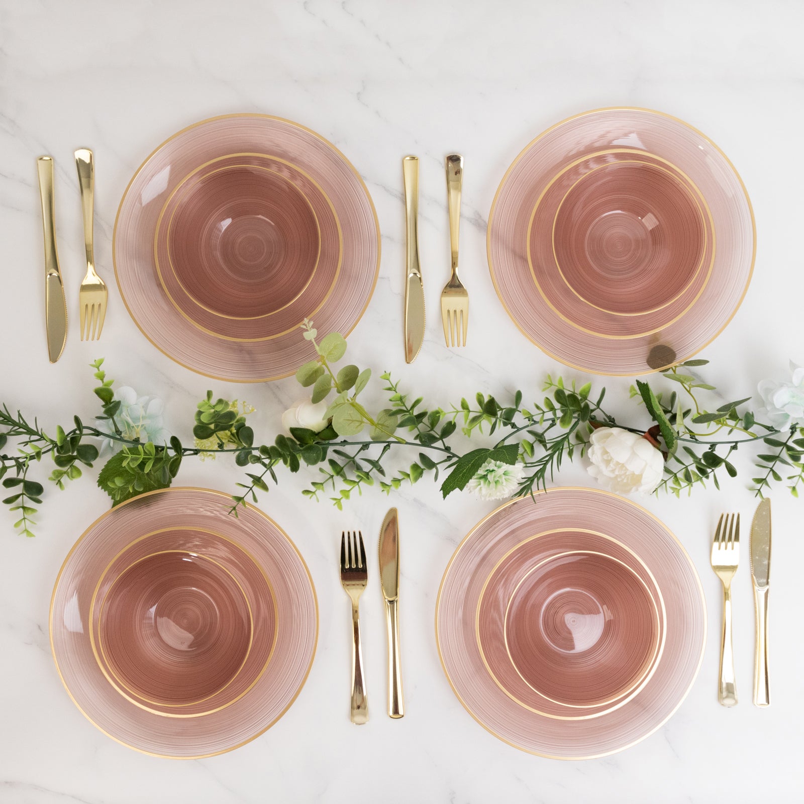 Transparent dusty rose bowls with gold rim on a marble table setting.