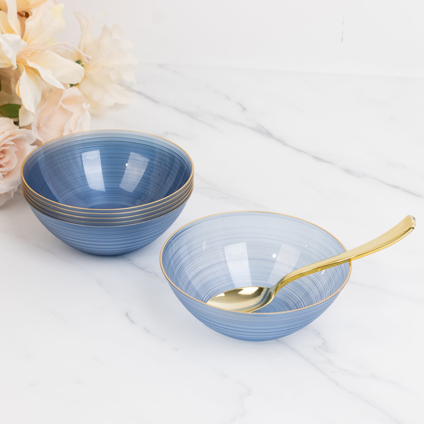 Transparent dusty blue bowls with gold rim on a marble surface.