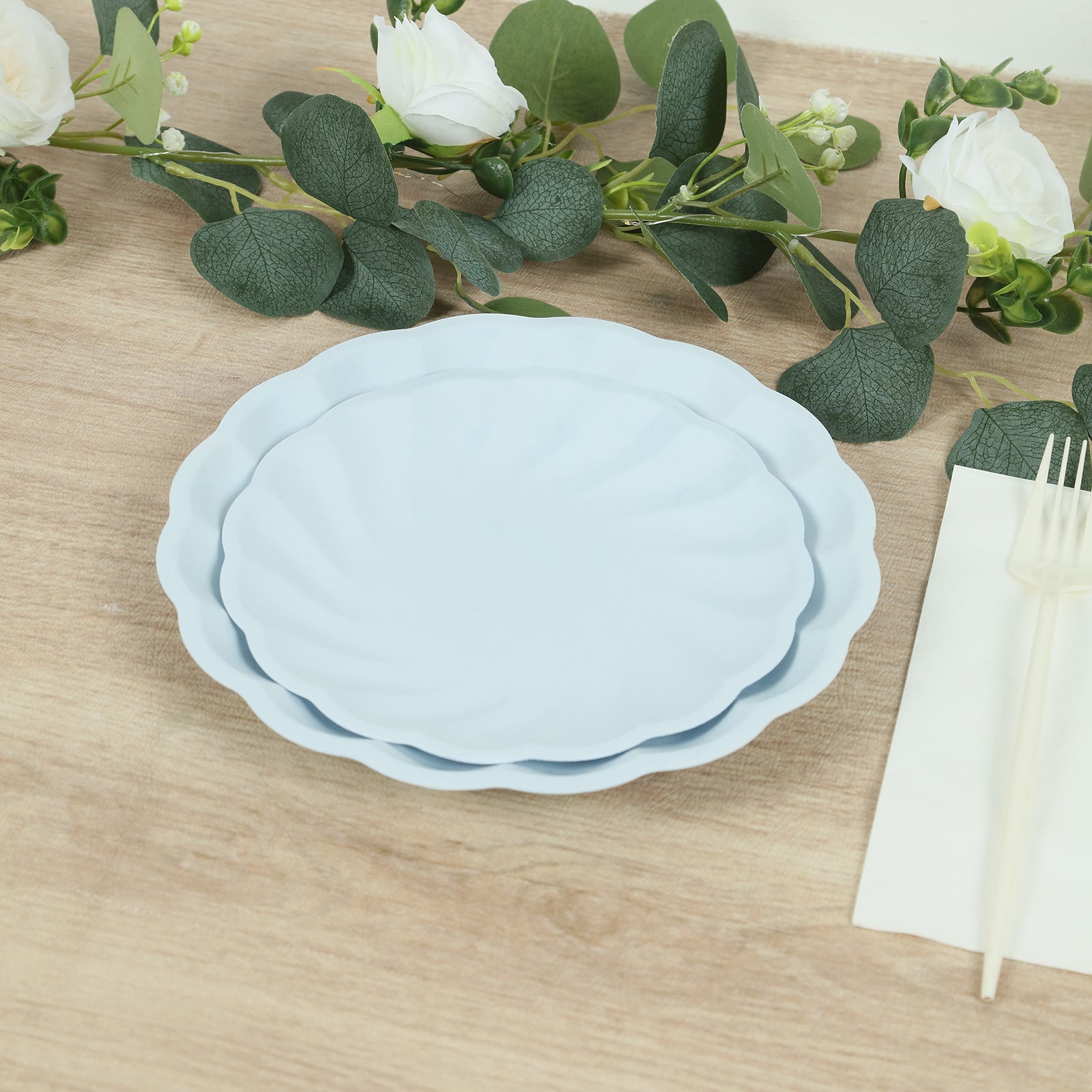 Light blue biodegradable salad plates with scalloped edges on a wooden table.