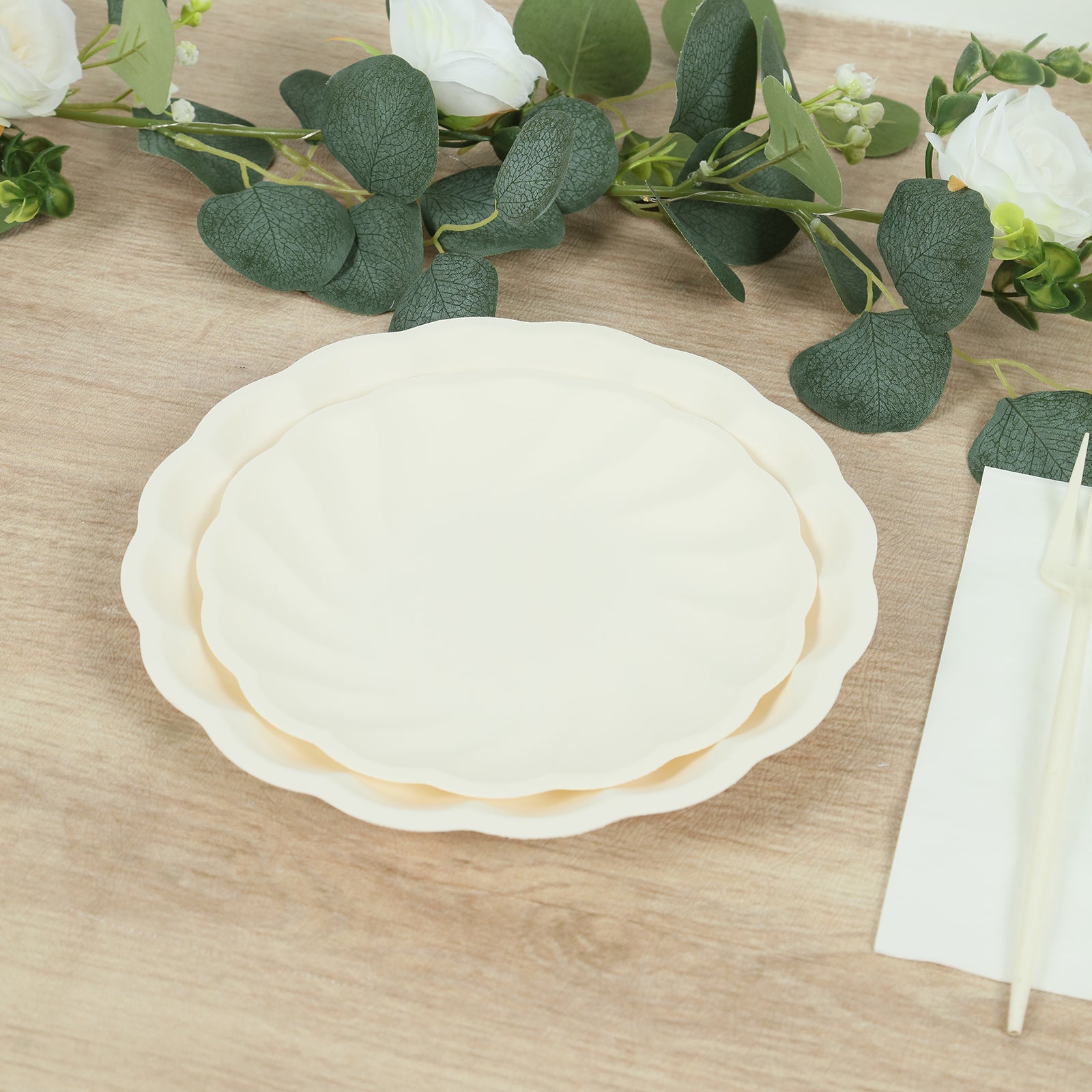 Cream biodegradable salad plates with swirl scalloped design on a wooden table.