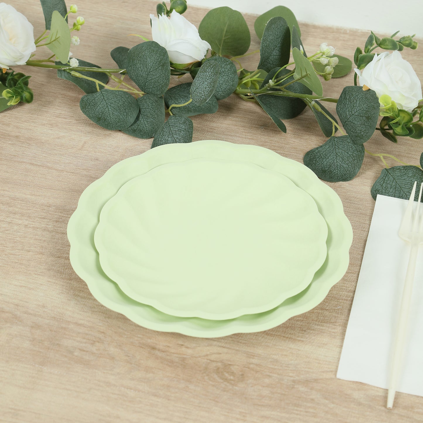 Sage green biodegradable salad plates stacked on a wooden table.