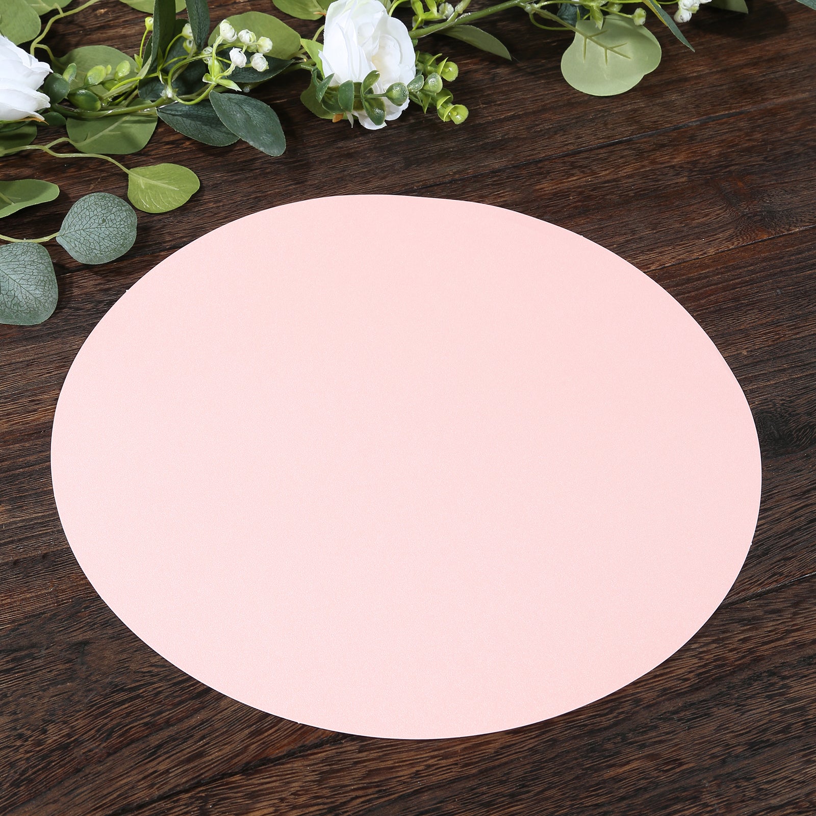 Pink round disposable paper placemat on a wooden table.
