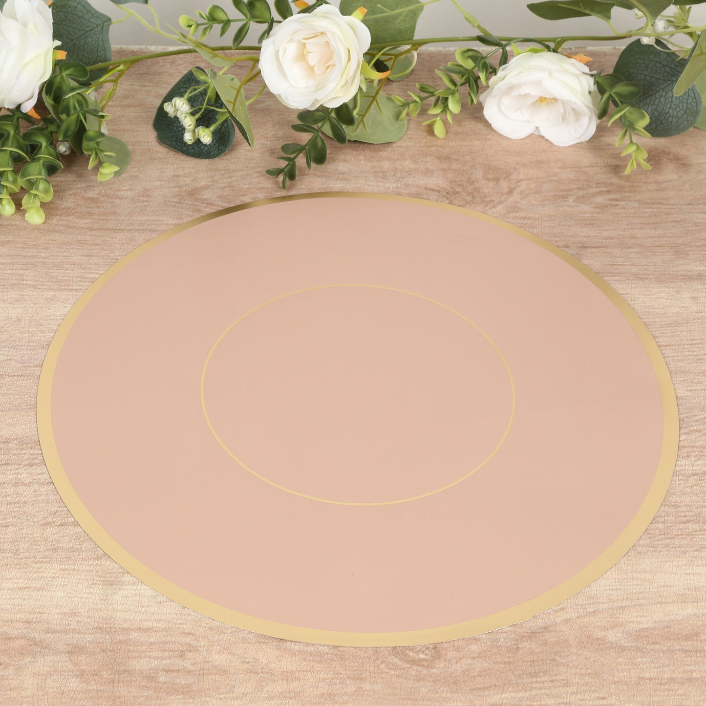 Dusty rose round disposable placemat with gold rim on a wooden surface.