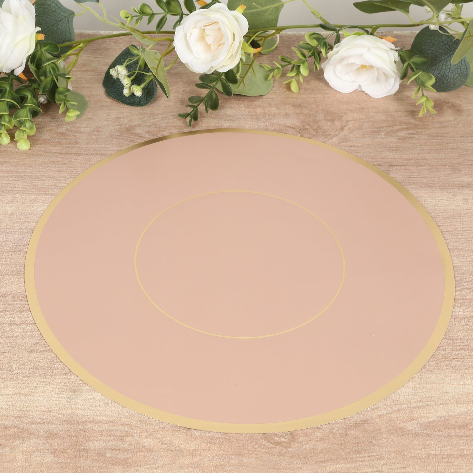 Dusty rose round disposable placemat with gold rim on a wooden surface.