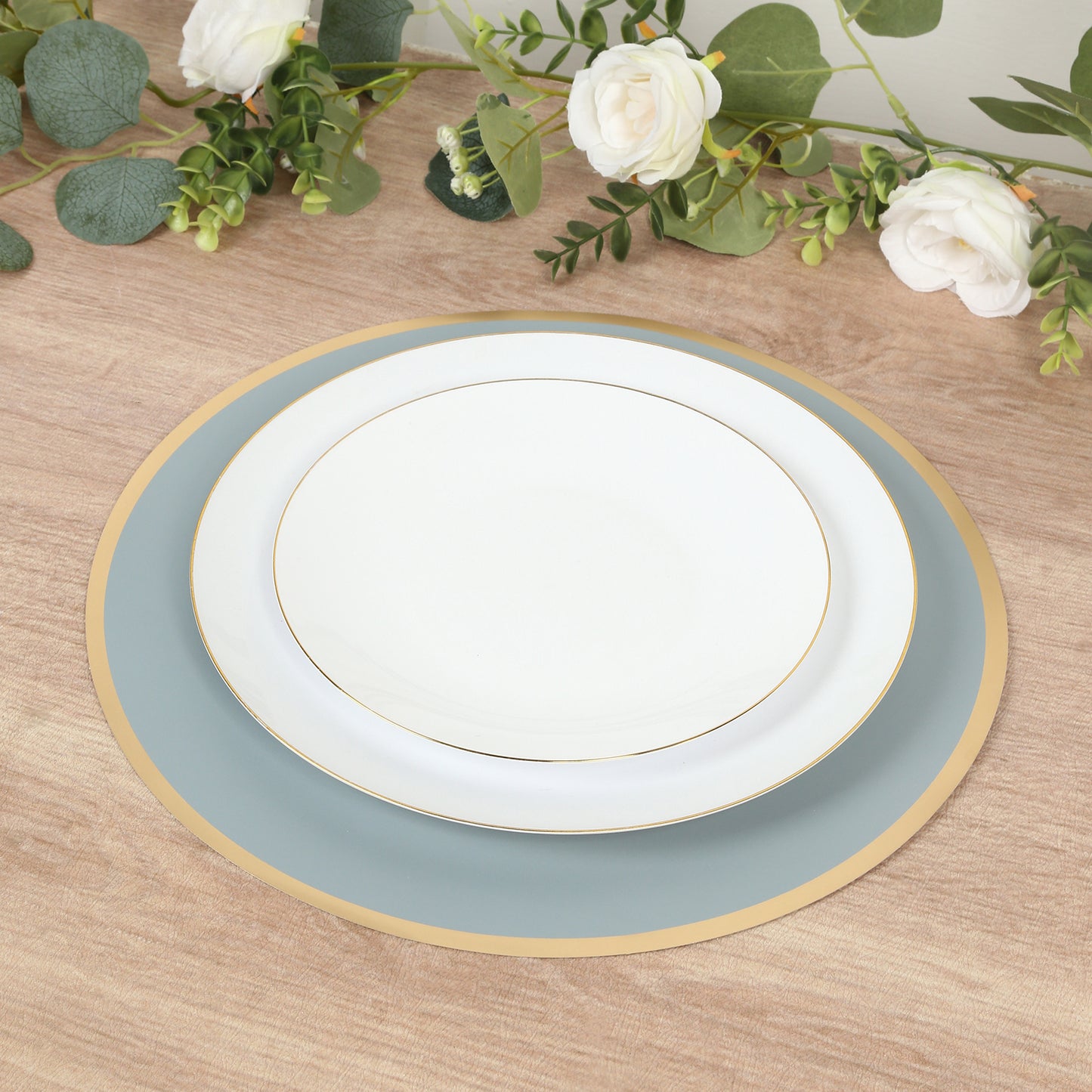 Dusty blue round disposable placemats with gold rim on a wooden table.
