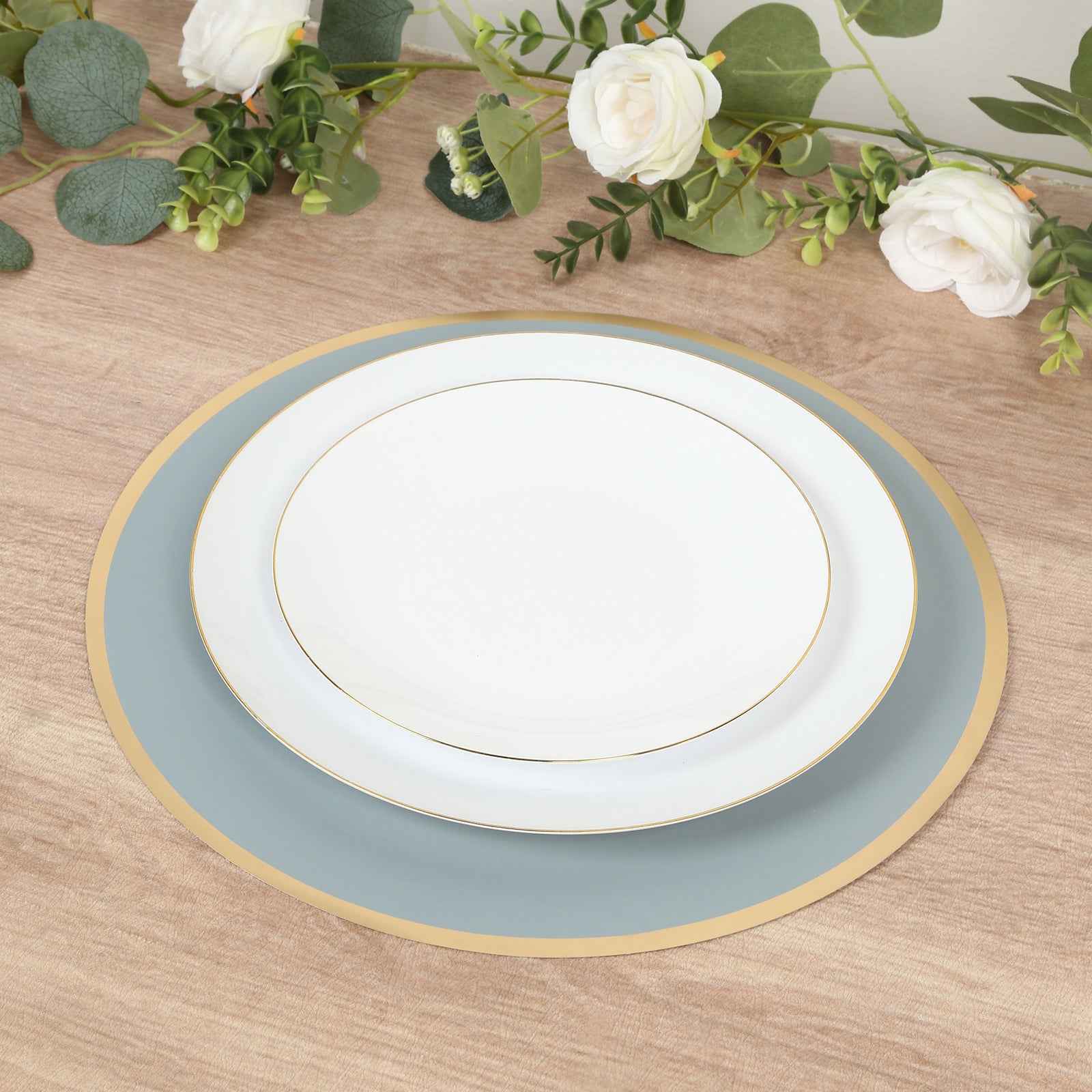 Dusty blue round disposable placemats with gold rim on a wooden table.