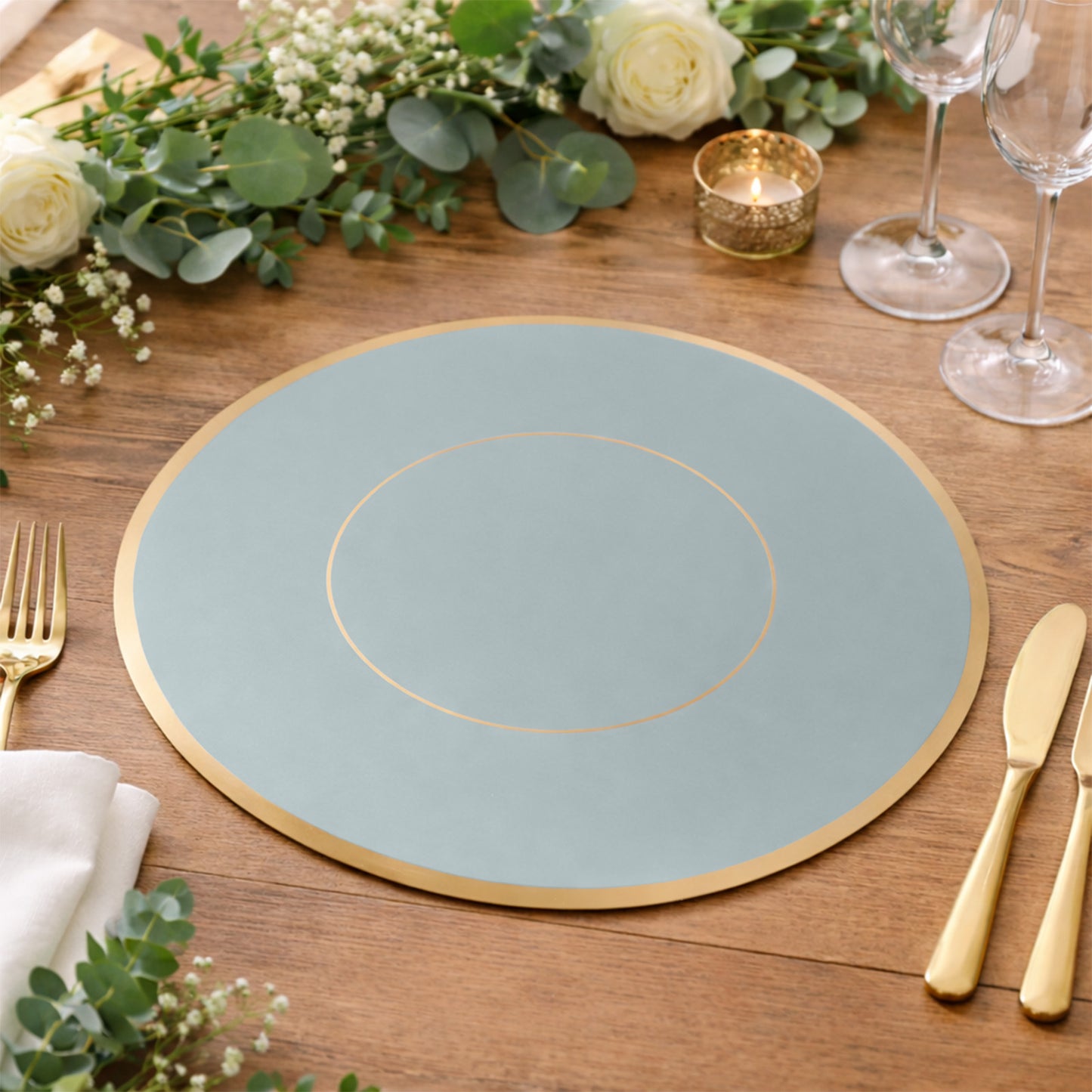 Dusty blue round disposable table placemat with gold rim on a wooden table.