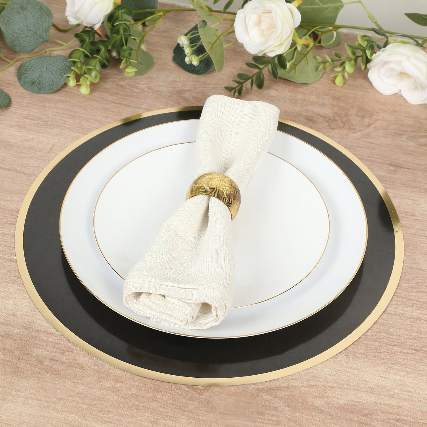 Black round disposable placemat with gold rim and white plate on wooden table.