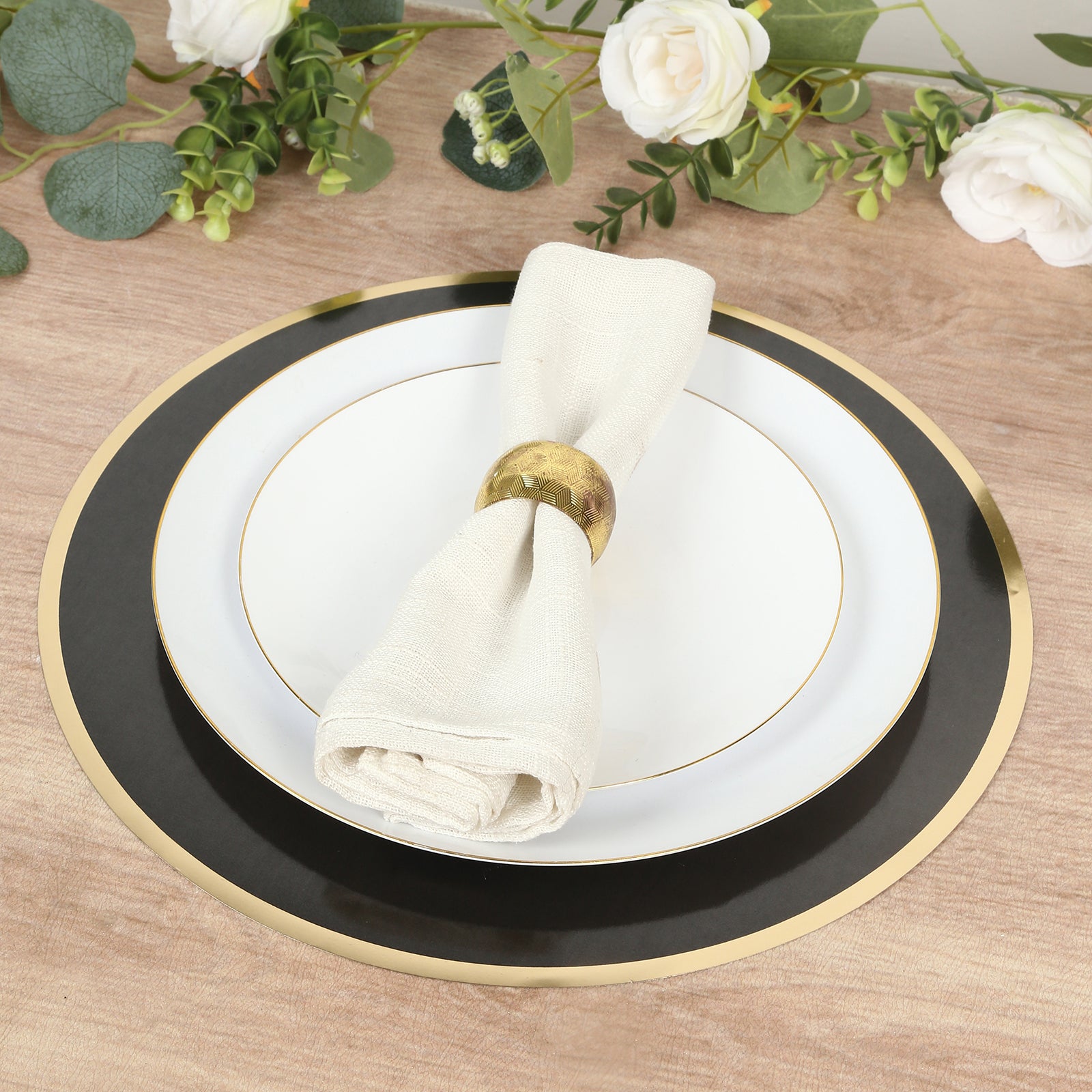 Black round disposable placemat with gold rim and white plate on wooden table.