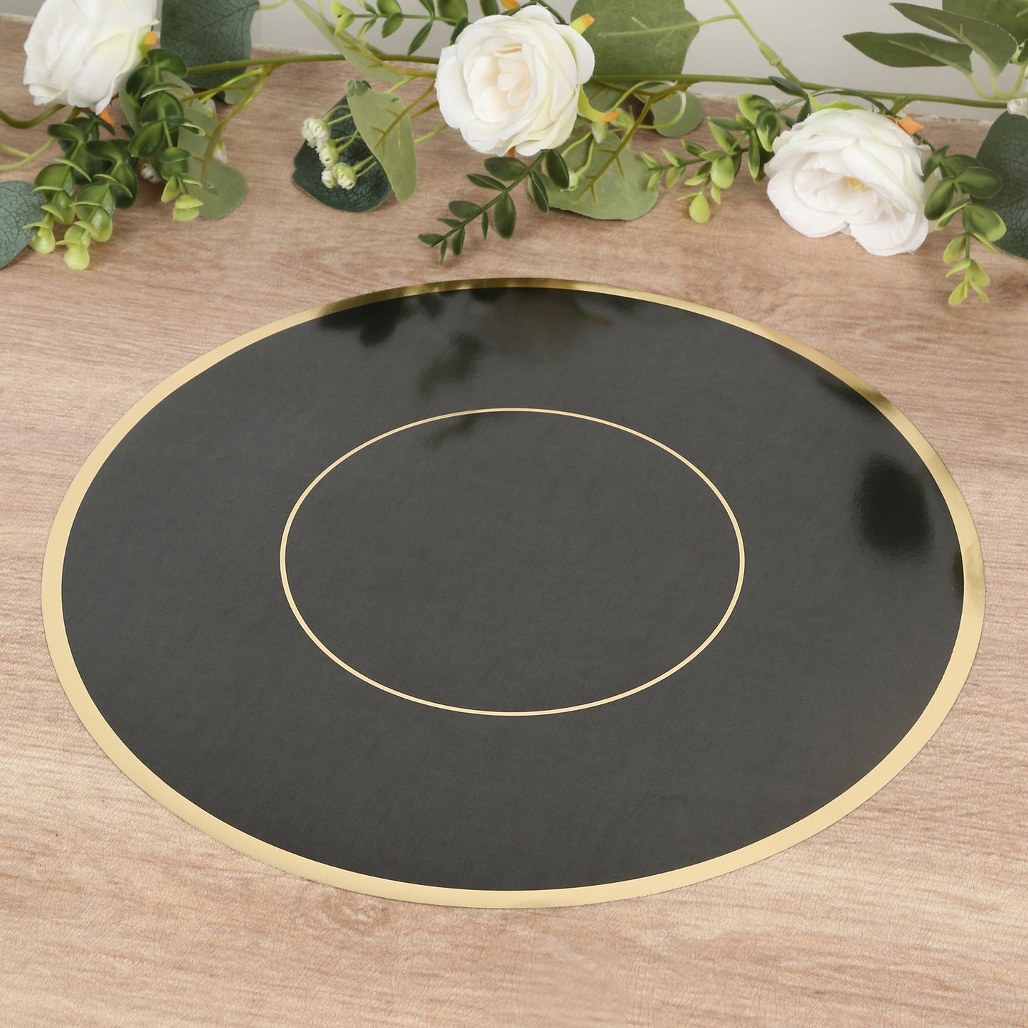Black round disposable table placemat with gold rim on a wooden surface.