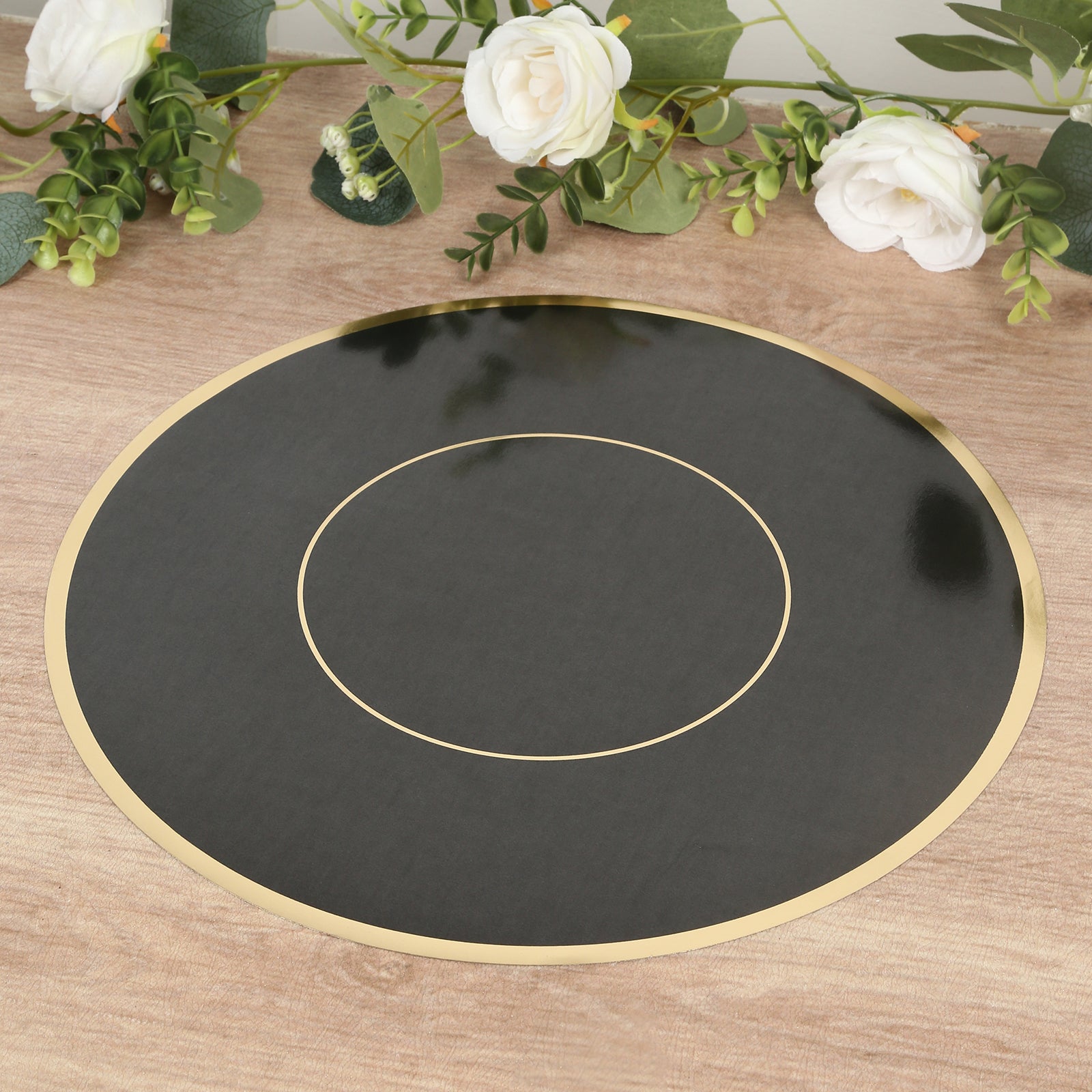 Black round disposable table placemat with gold rim on a wooden surface.