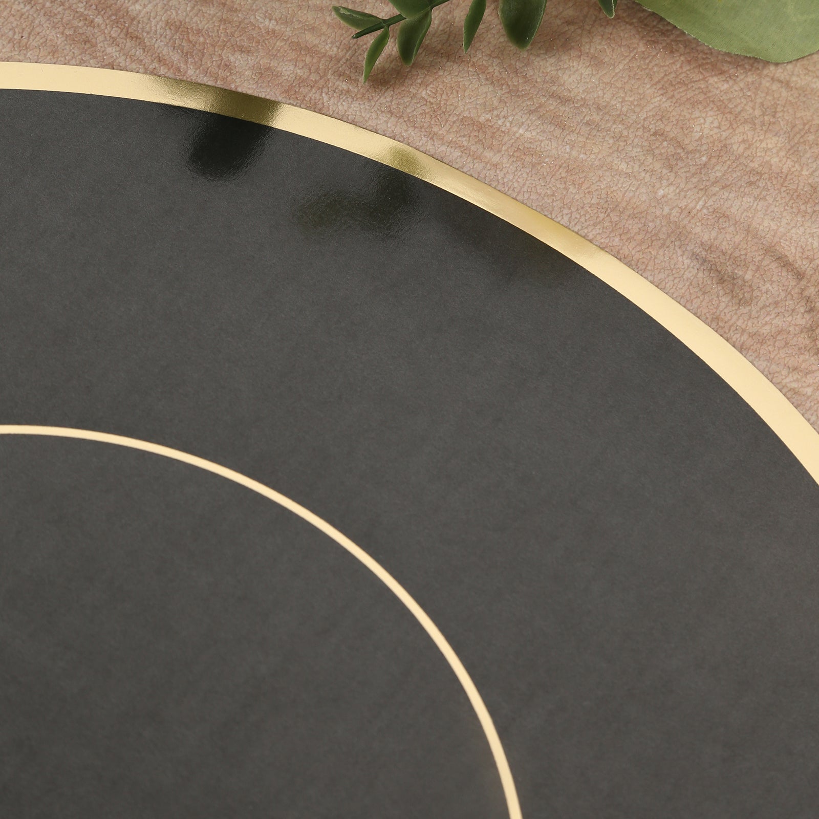Black round disposable placemat with gold rim on textured surface.