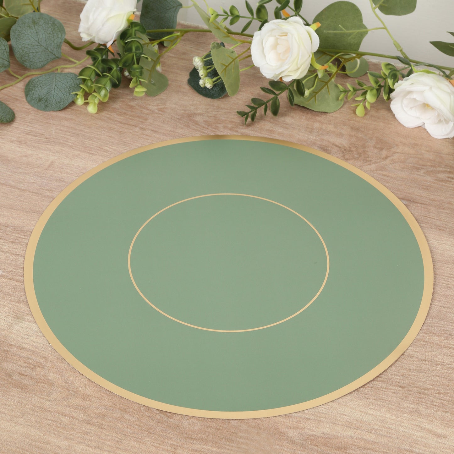 Sage green round disposable table placemat with gold rim on a wooden surface.