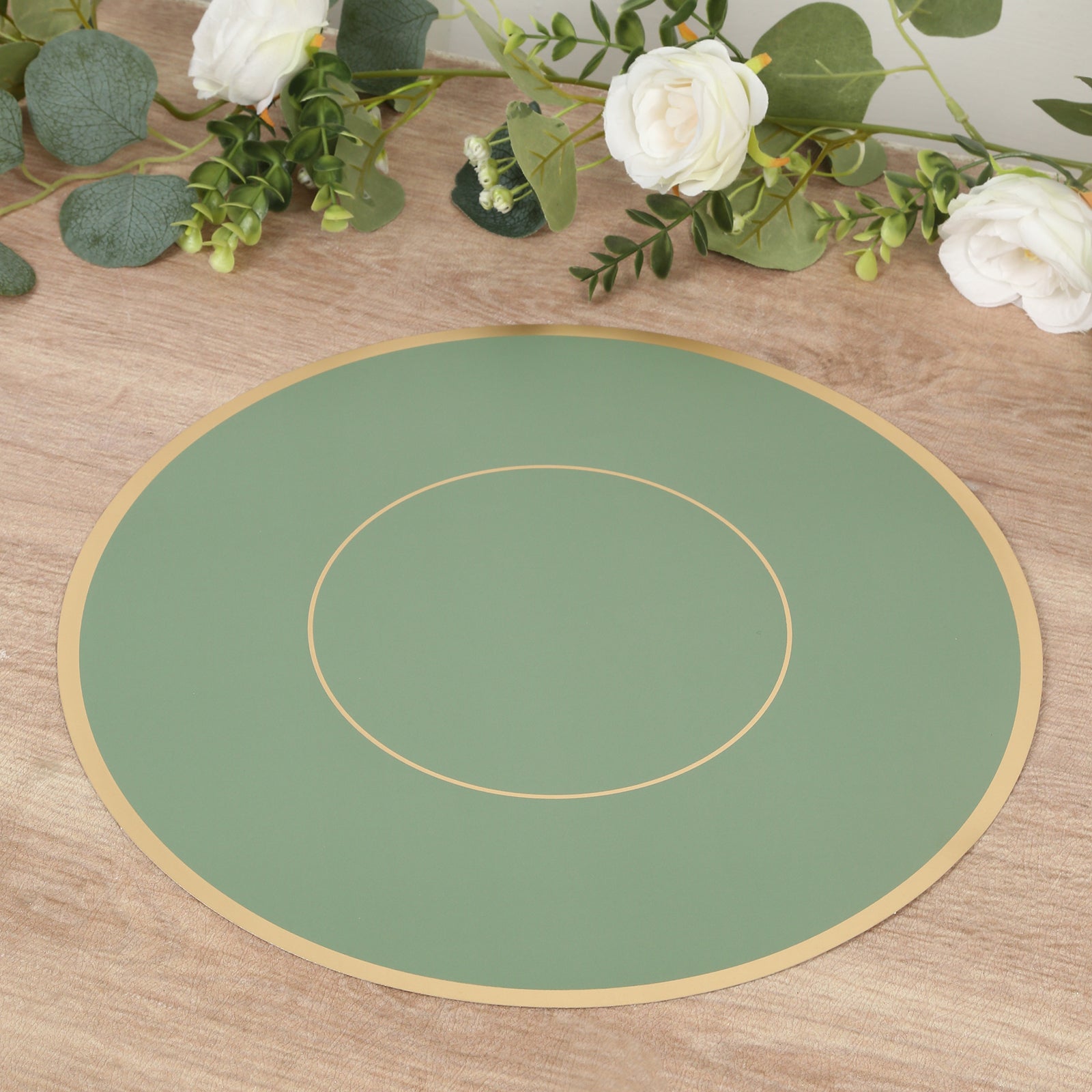 Sage green round disposable table placemat with gold rim on a wooden surface.