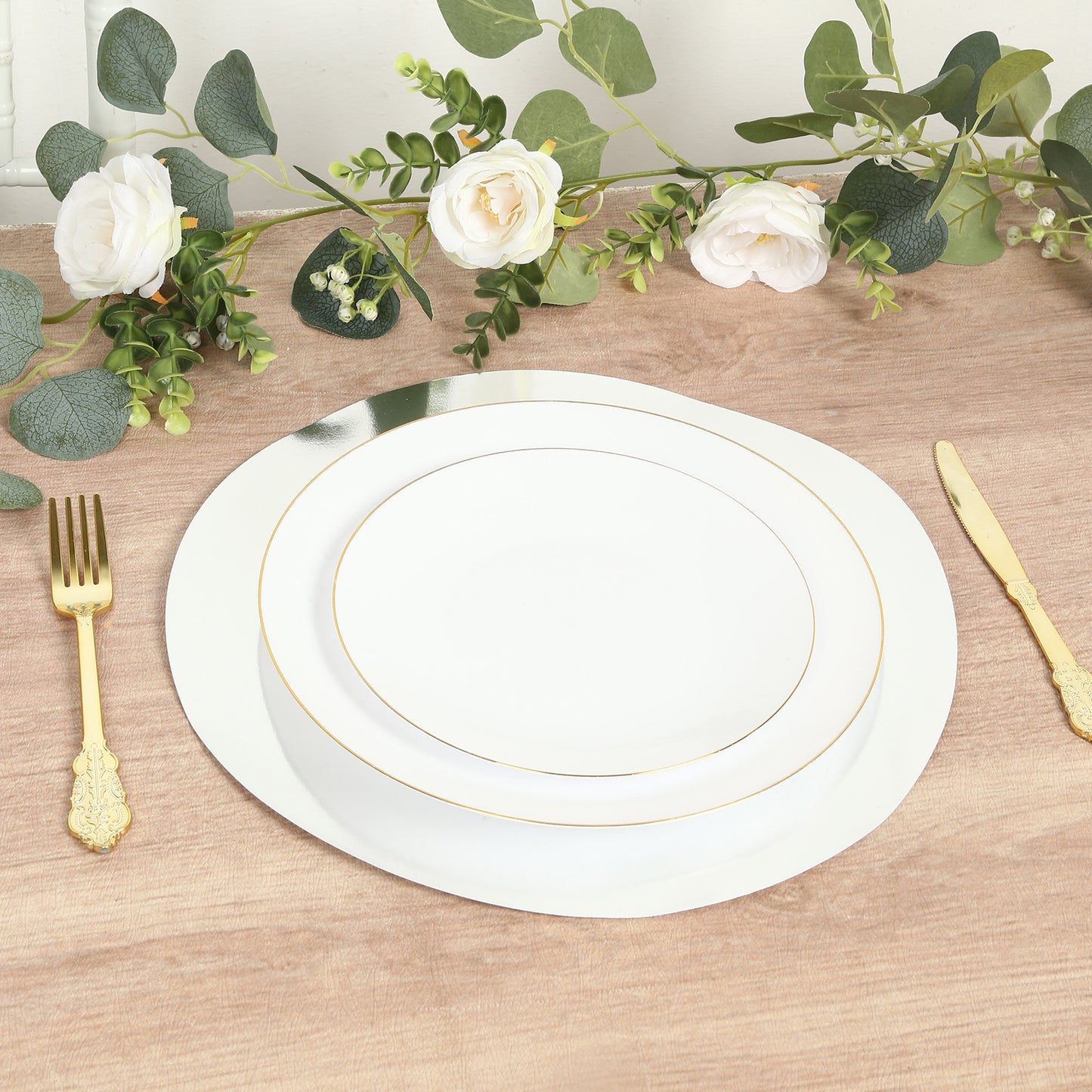 Silver round disposable table placemats on a wooden table with decorative foliage.