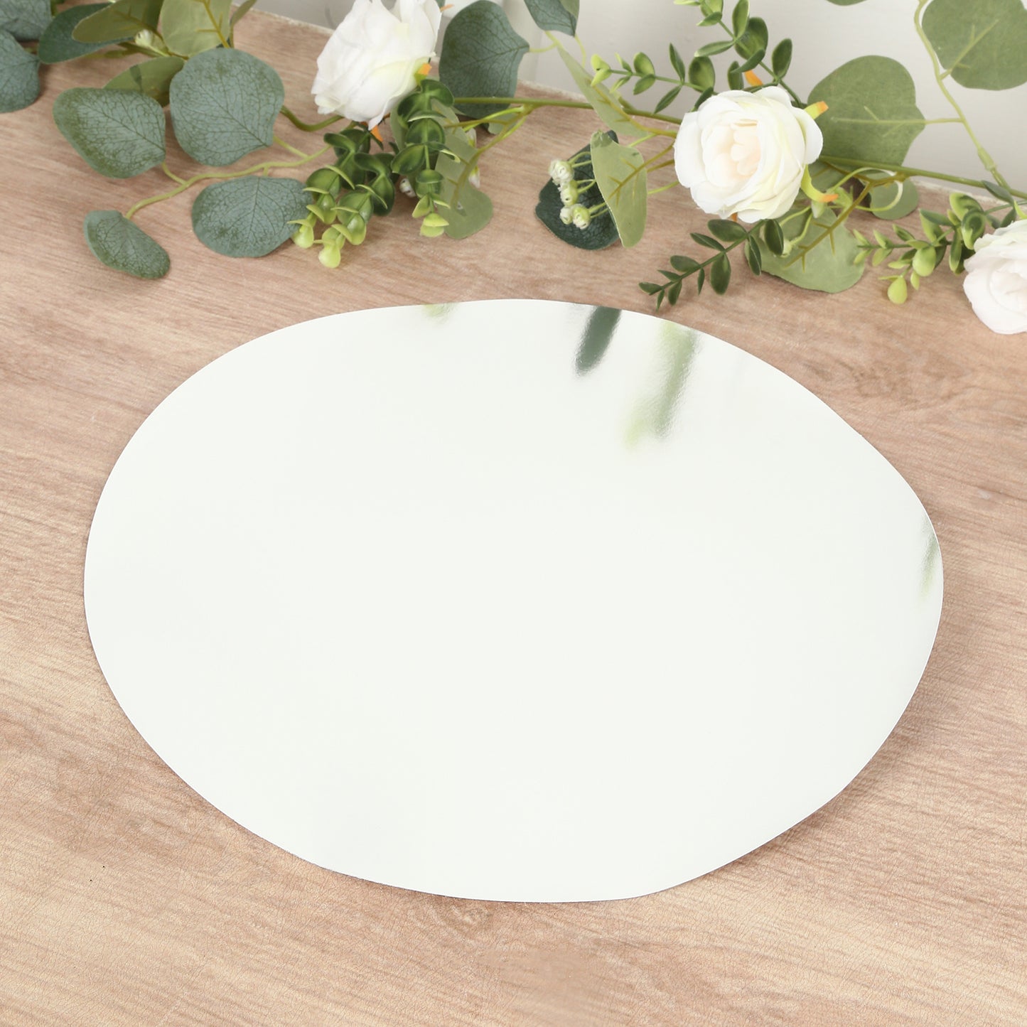 Silver round disposable table placemat on a wooden surface with greenery.