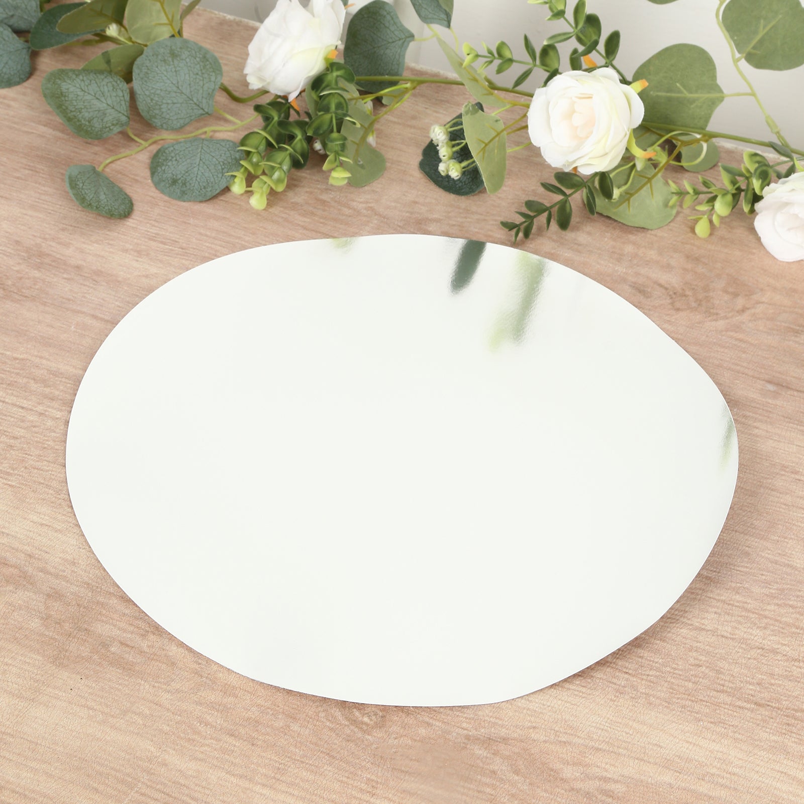 Silver round disposable table placemat on a wooden surface with greenery.