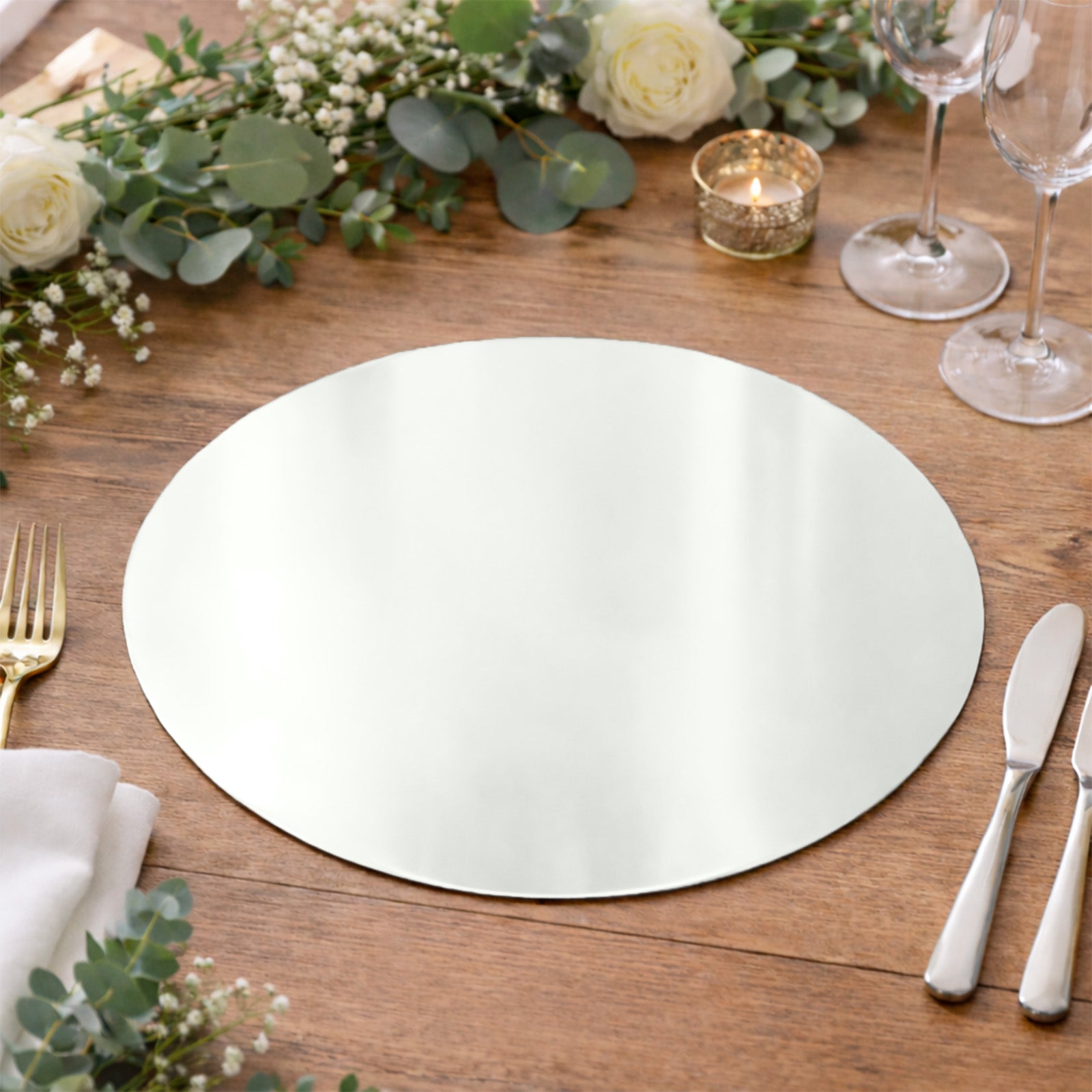 Silver round disposable placemat on a wooden table with floral decor.