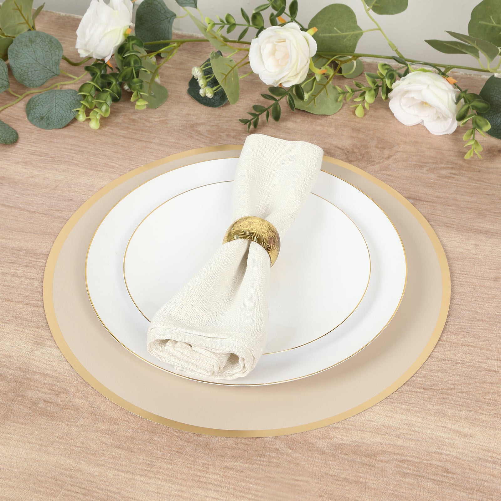 Taupe round disposable table placemats with gold rim on a wooden table setting.