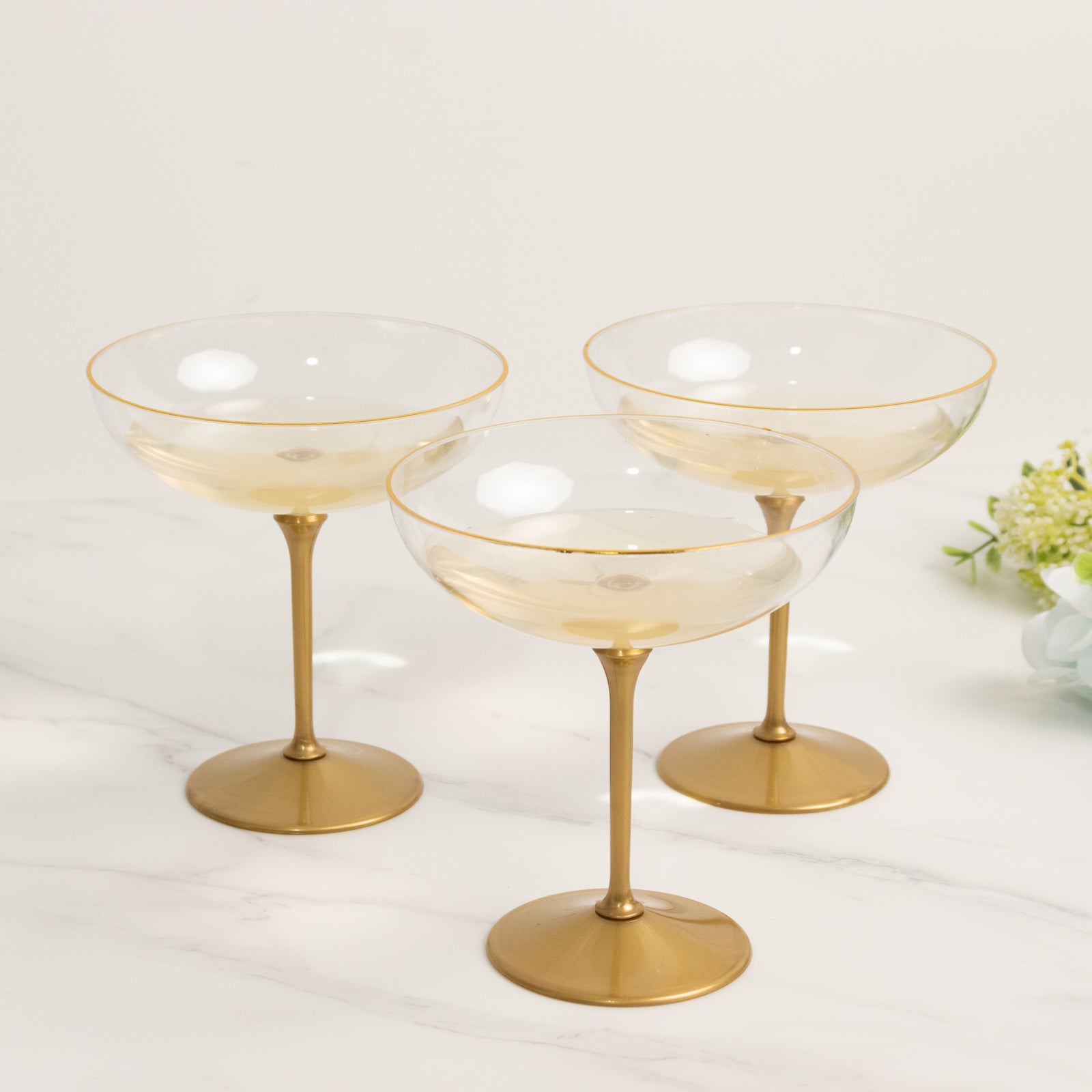 Set of three clear champagne coupes with gold stems for elegant serving.