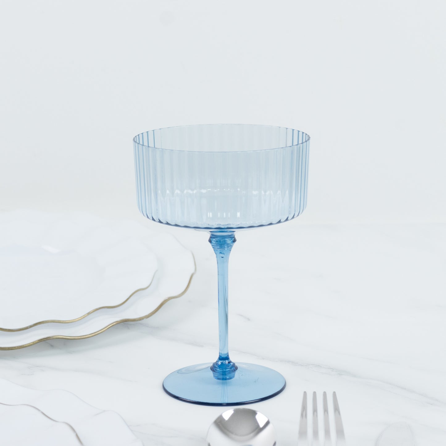 Dusty blue ribbed disposable coupe champagne glass on a marble surface.