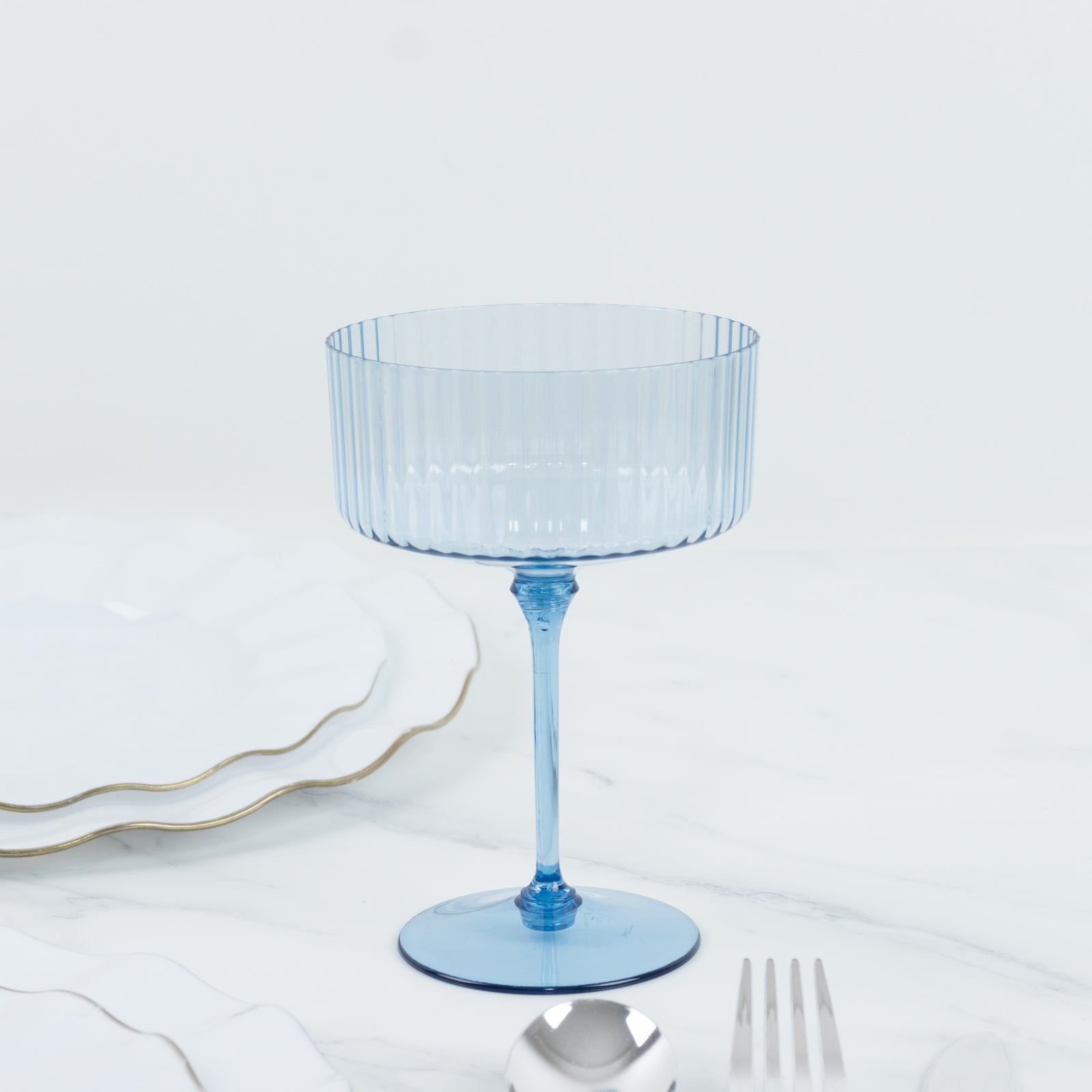 Dusty blue ribbed disposable coupe champagne glass on a marble surface.