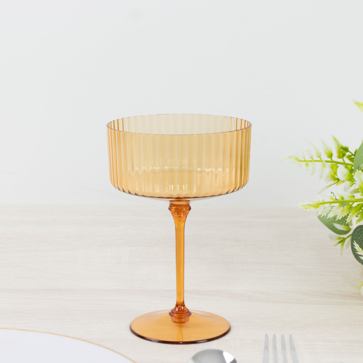 Amber gold disposable cocktail glass with ribbed design on a light table.