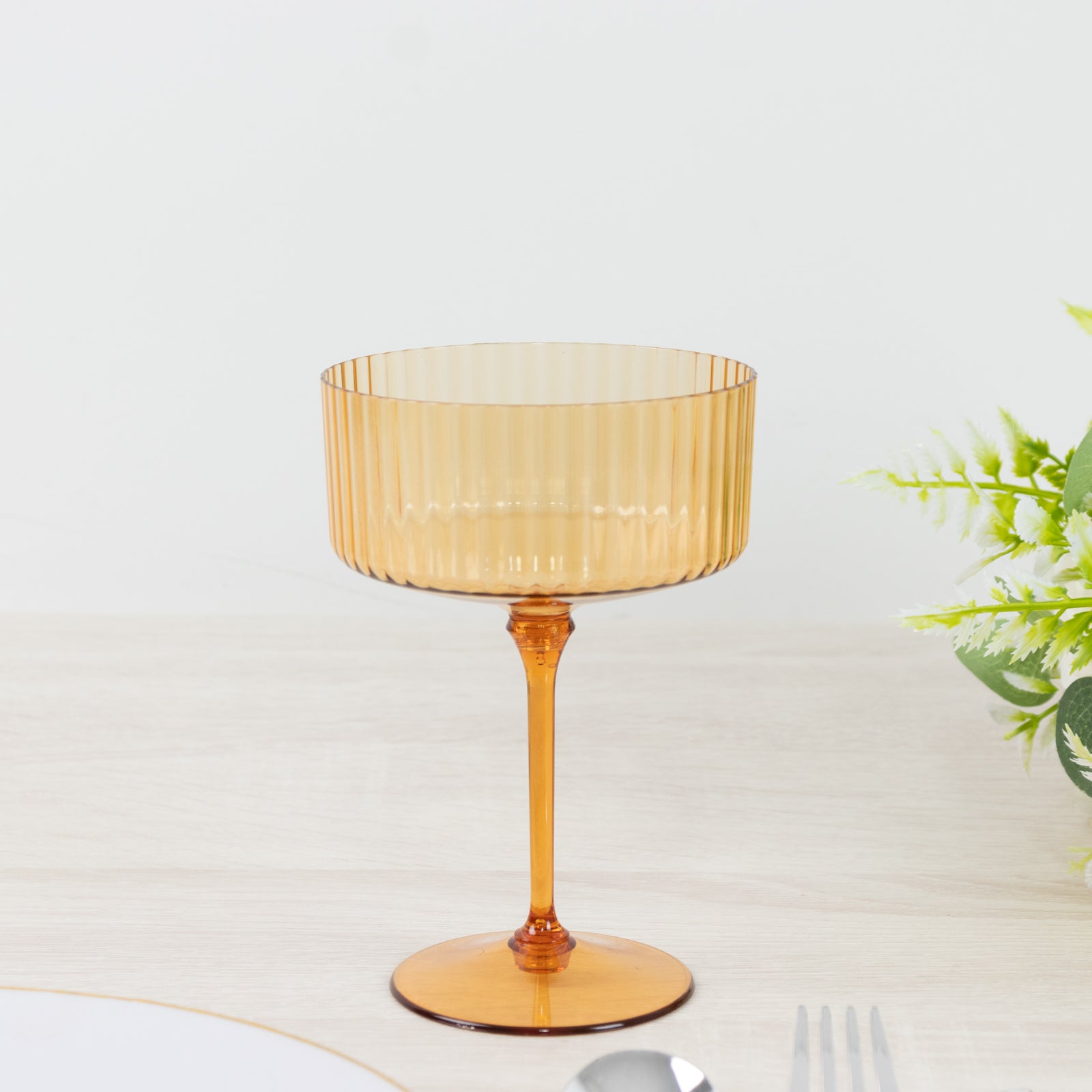 Amber gold disposable cocktail glass with ribbed design on a light table.