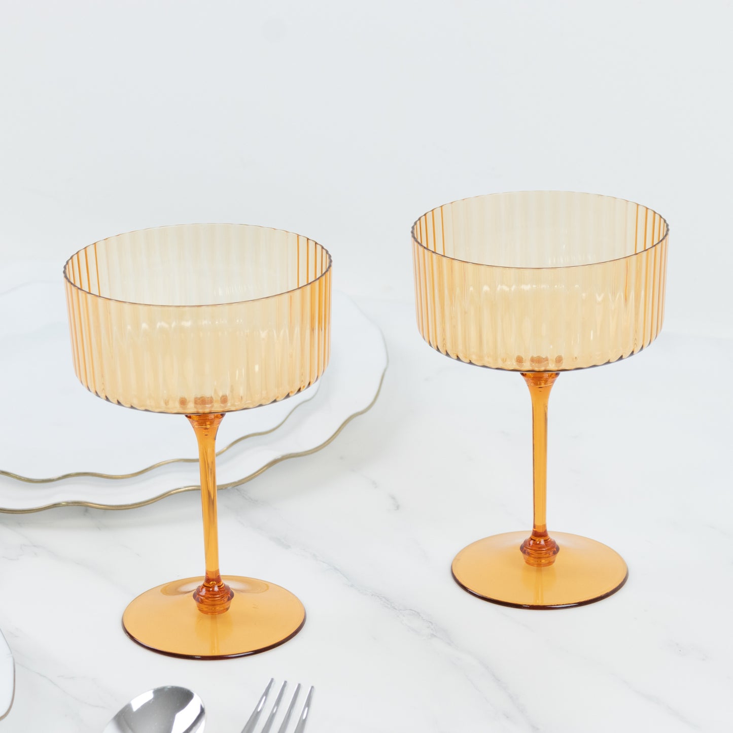 Amber gold ribbed disposable cocktail glasses on a marble surface.