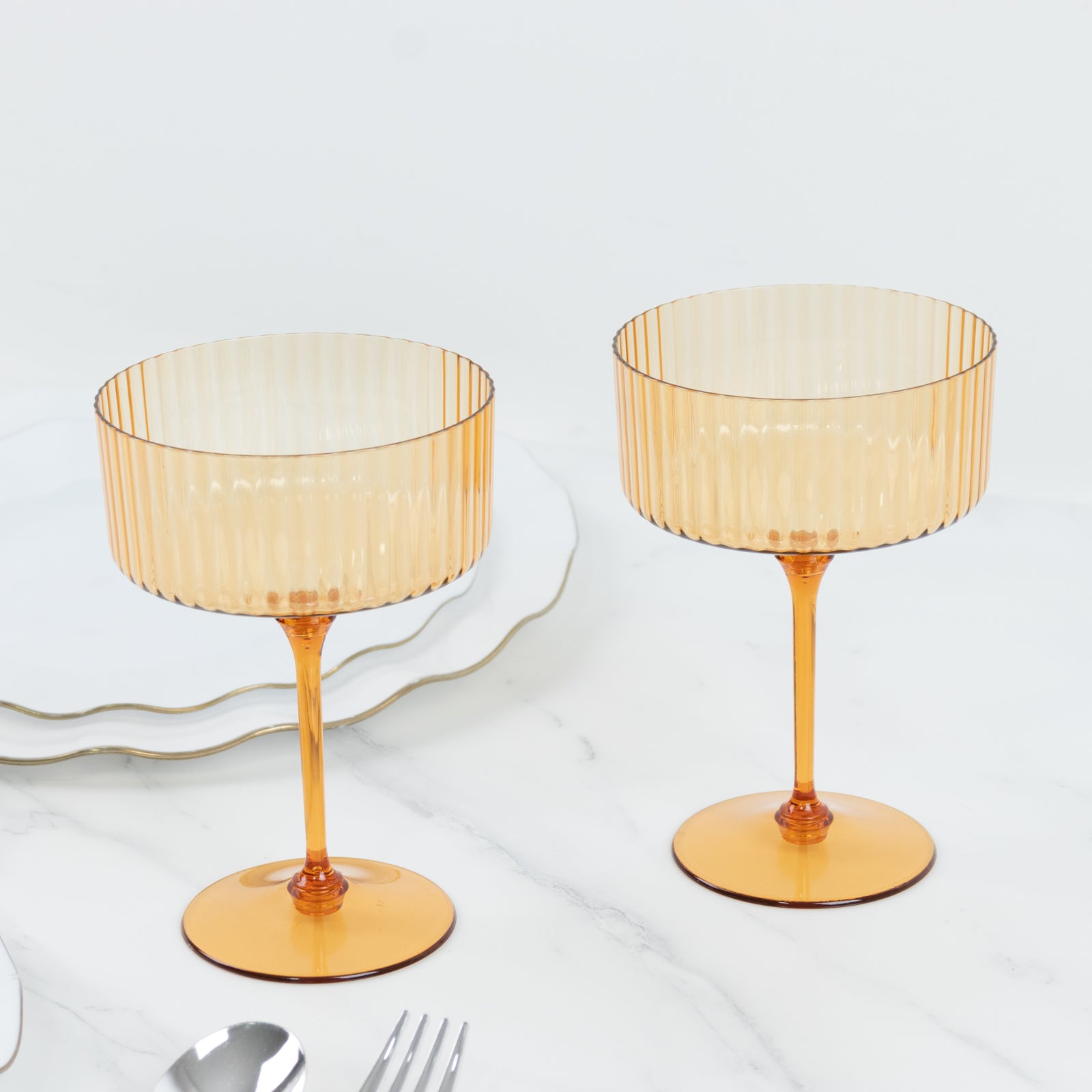 Amber gold ribbed disposable cocktail glasses on a marble surface.