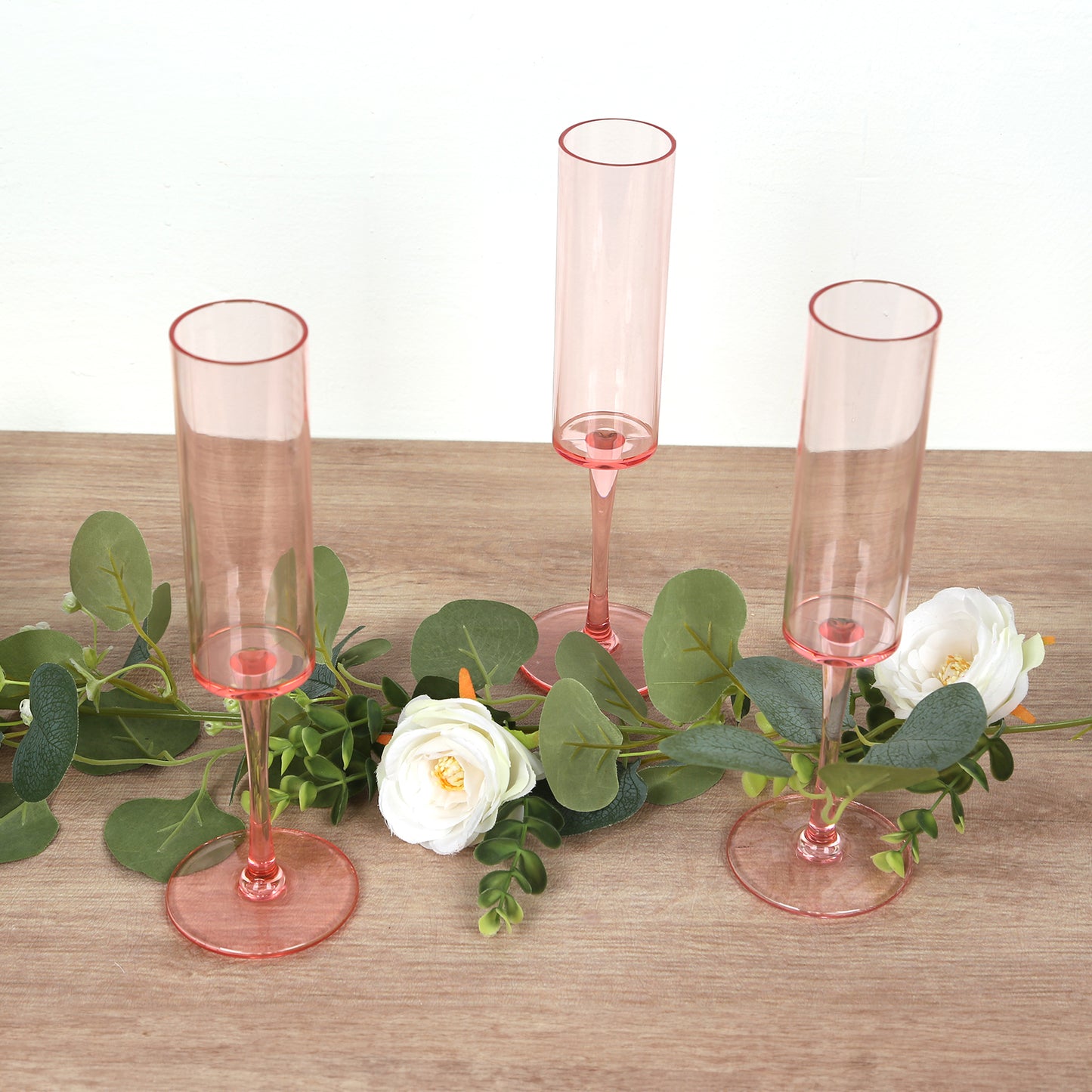 Transparent blush reusable plastic champagne flute glasses arranged with greenery and flowers.