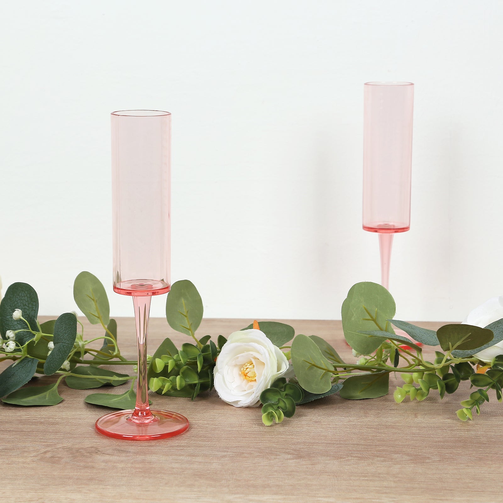 Transparent blush champagne flutes with long stems and floral decor.
