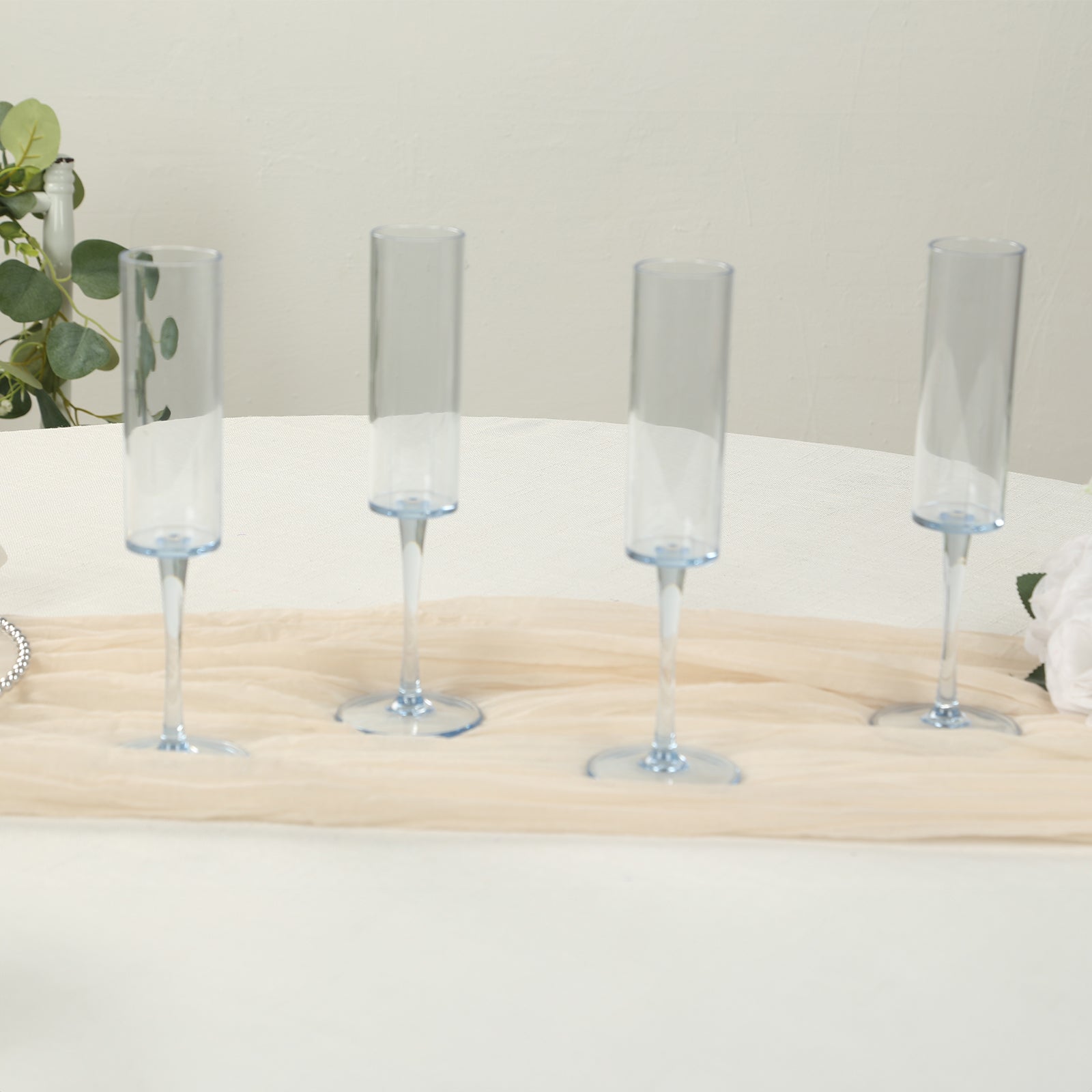 Transparent dusty blue reusable plastic champagne flutes with long stems.