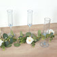 Transparent dusty blue champagne flutes on a wooden surface with greenery and flowers.