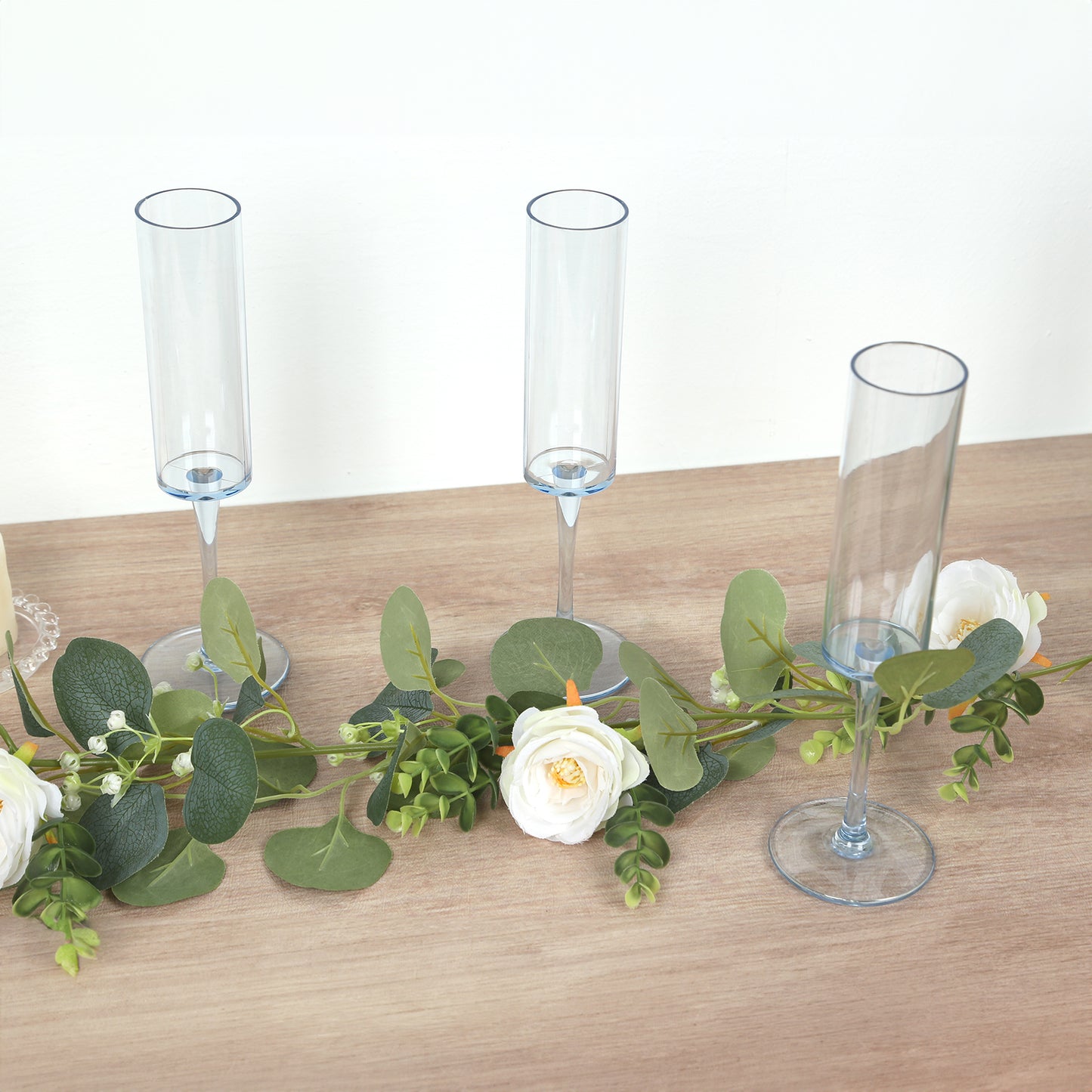Transparent dusty blue champagne flutes on a wooden surface with greenery and flowers.