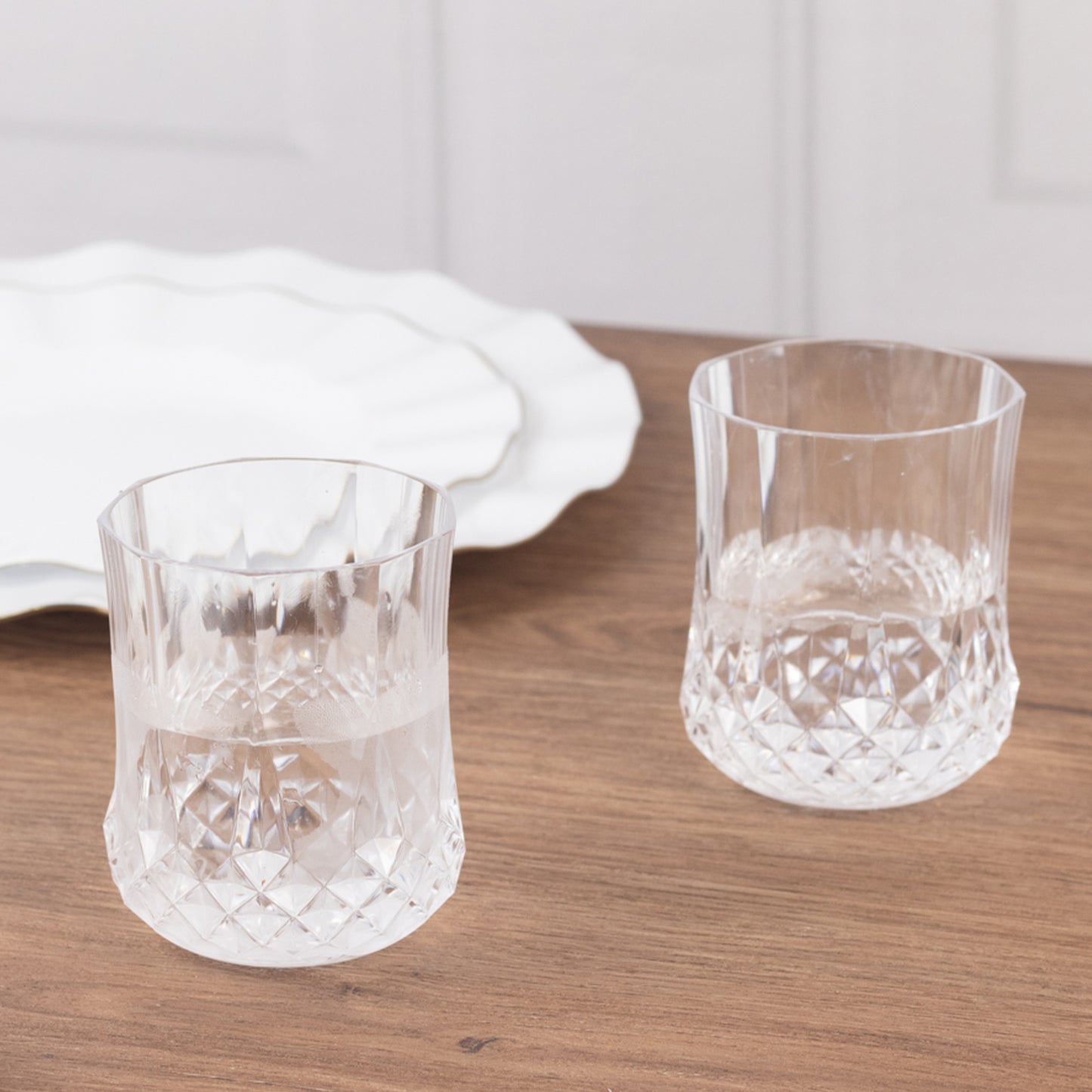 Clear crystal cut plastic stemless wine glasses on a wooden table.