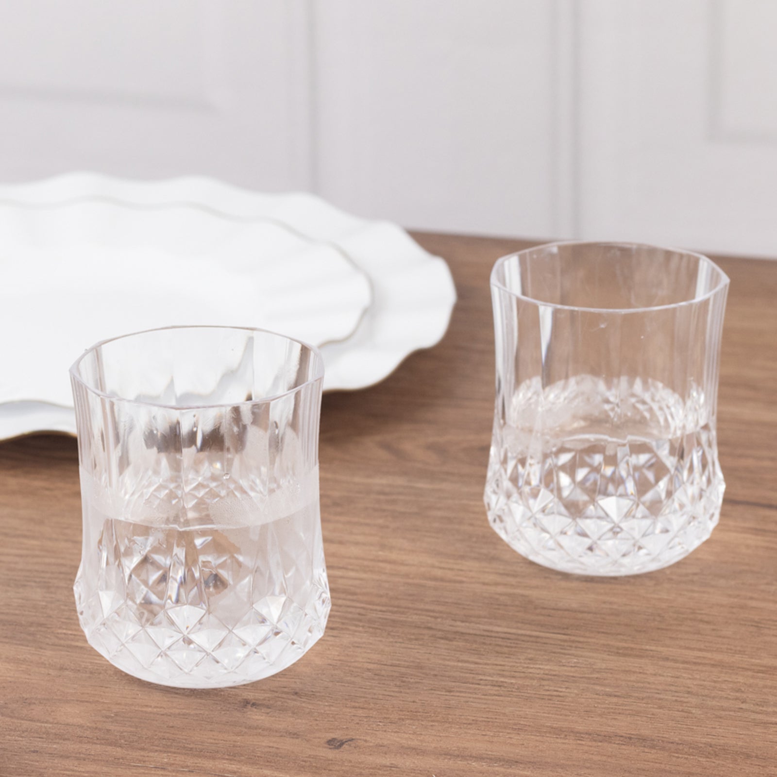 Clear crystal cut plastic stemless wine glasses on a wooden table.