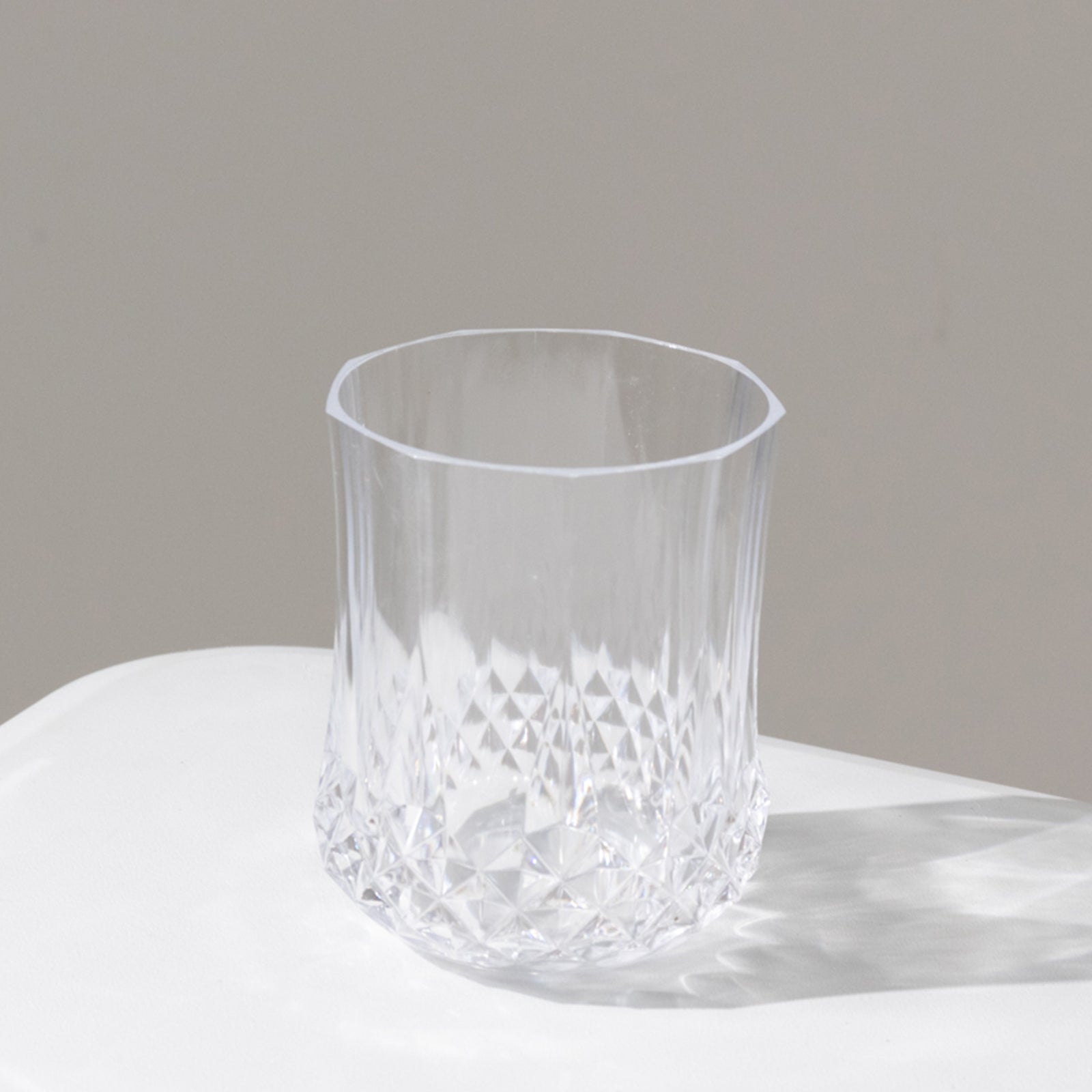 Clear crystal cut plastic stemless wine glass on a white surface.
