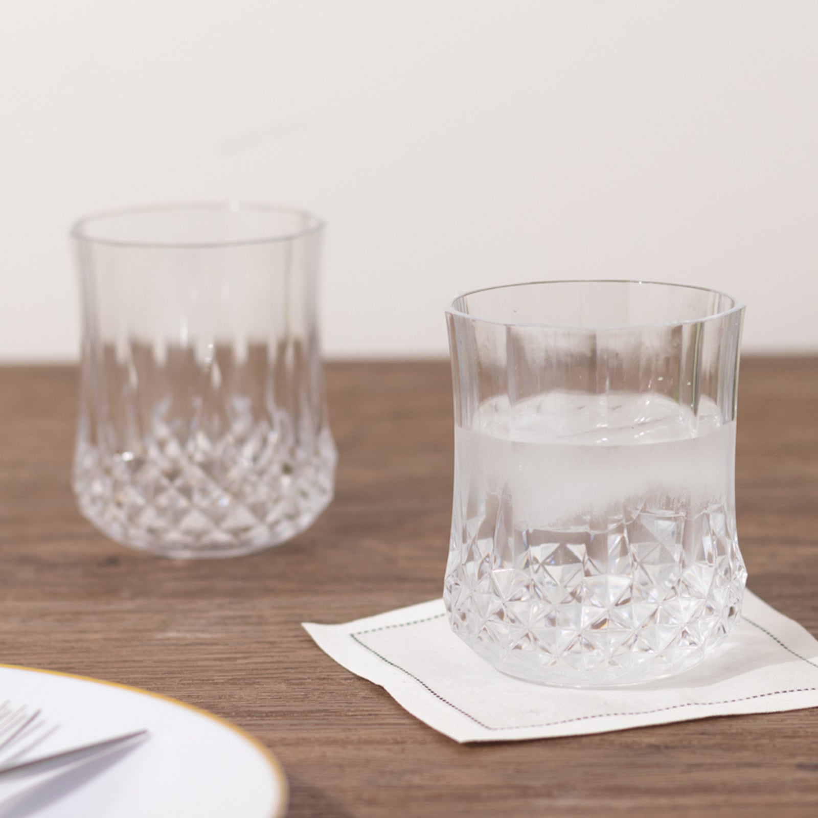 Clear crystal cut stemless wine glasses on a wooden table.