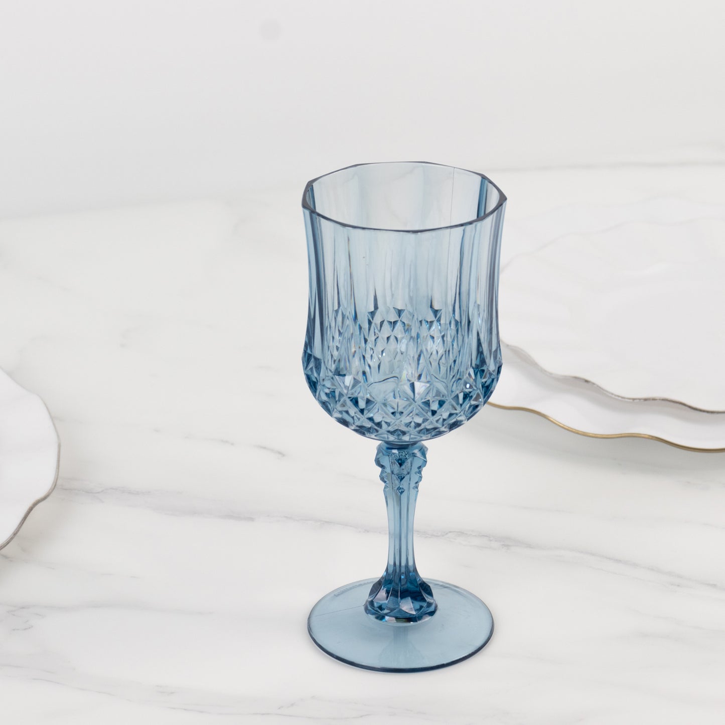 Dusty blue crystal cut reusable plastic cocktail goblet on a marble surface.