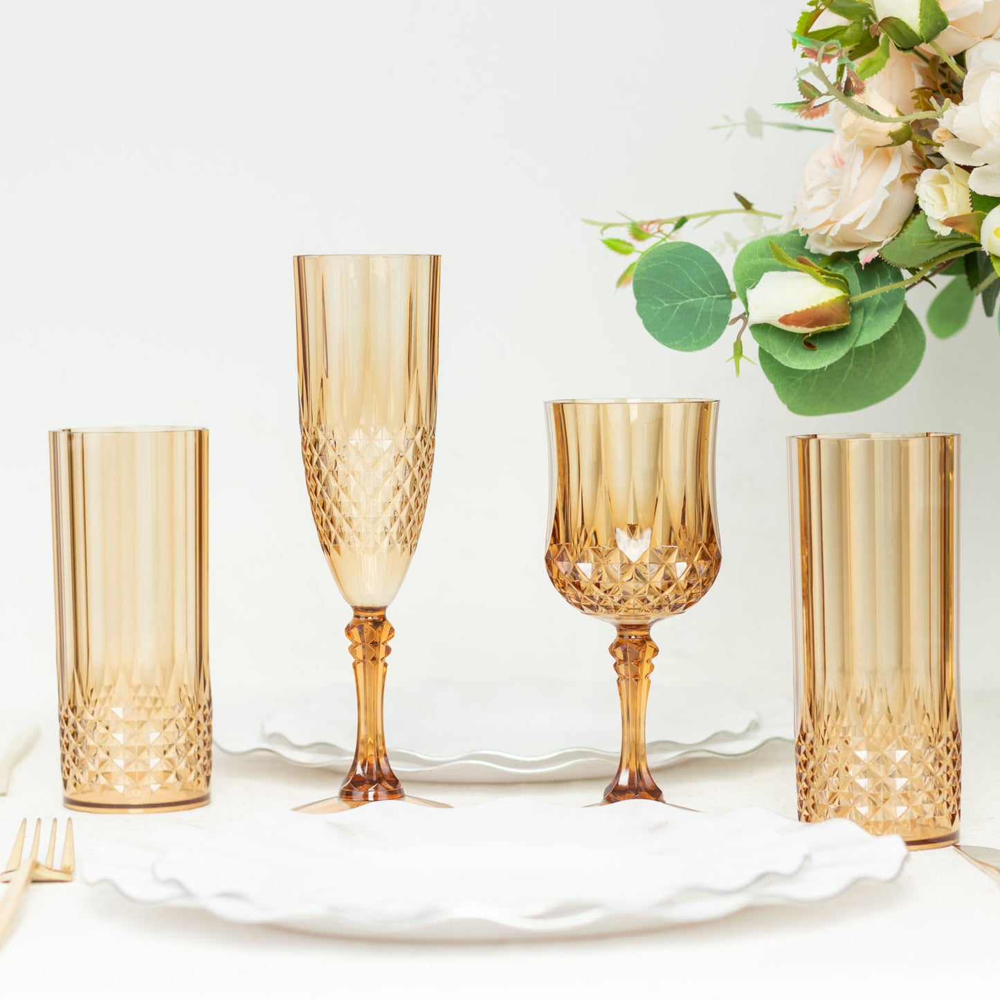 Amber gold reusable plastic cocktail goblets set on a table with flowers.