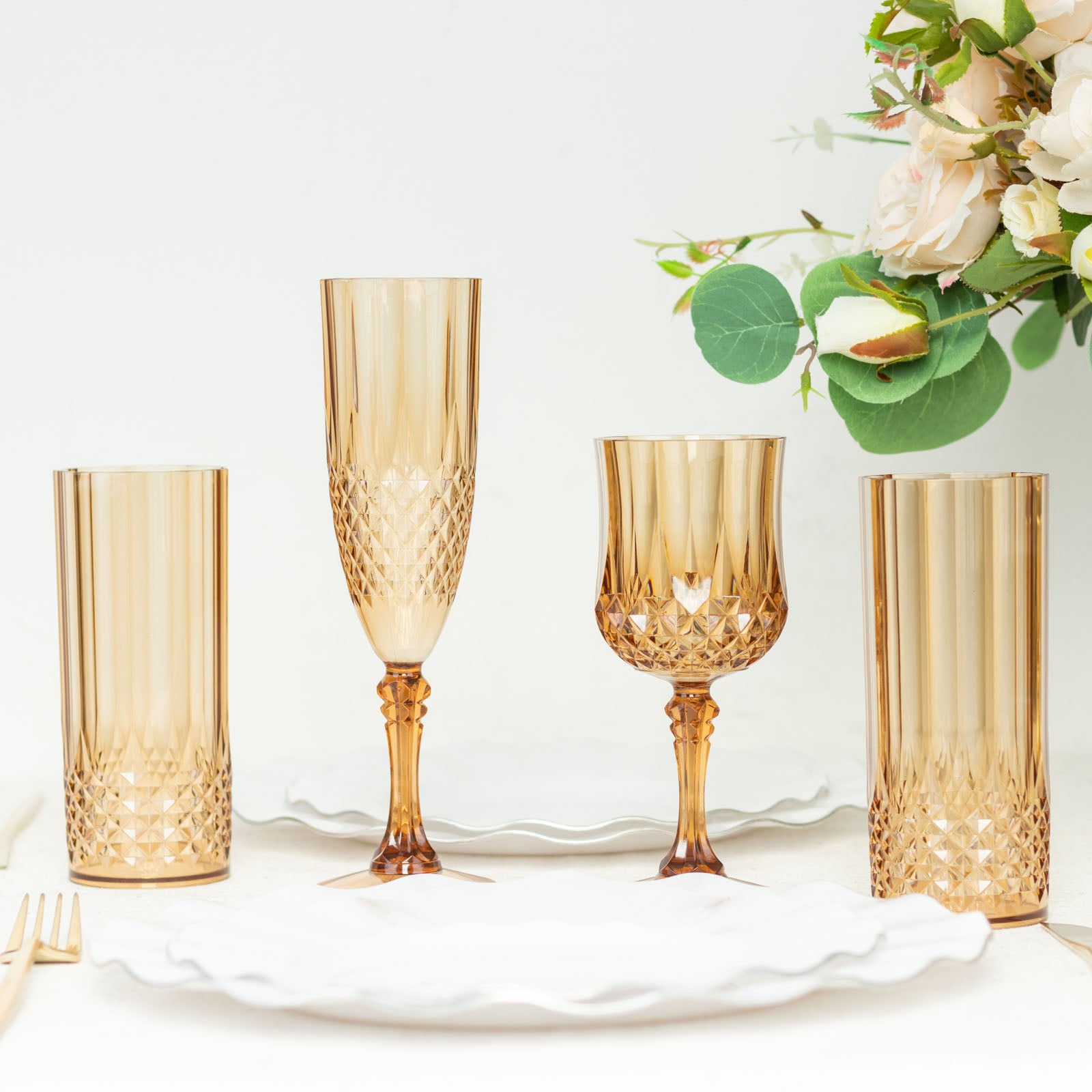 Amber gold reusable plastic cocktail goblets set on a table with flowers.