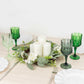 Assorted green crystal cut reusable plastic cocktail goblets on a table setting.