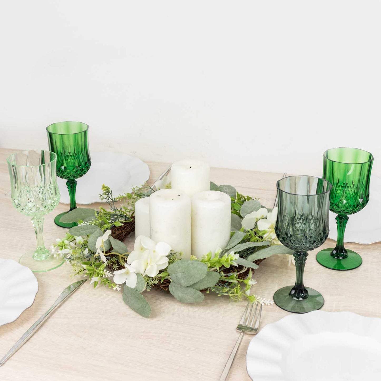 Assorted green crystal cut reusable plastic cocktail goblets on a table setting.