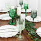 Assorted green crystal cut reusable plastic cocktail goblets on a dining table.