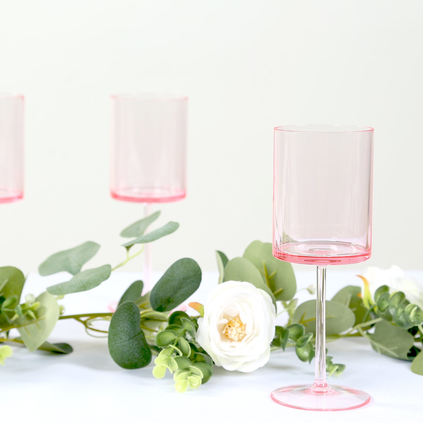 Transparent pink reusable cocktail glasses with long stems.