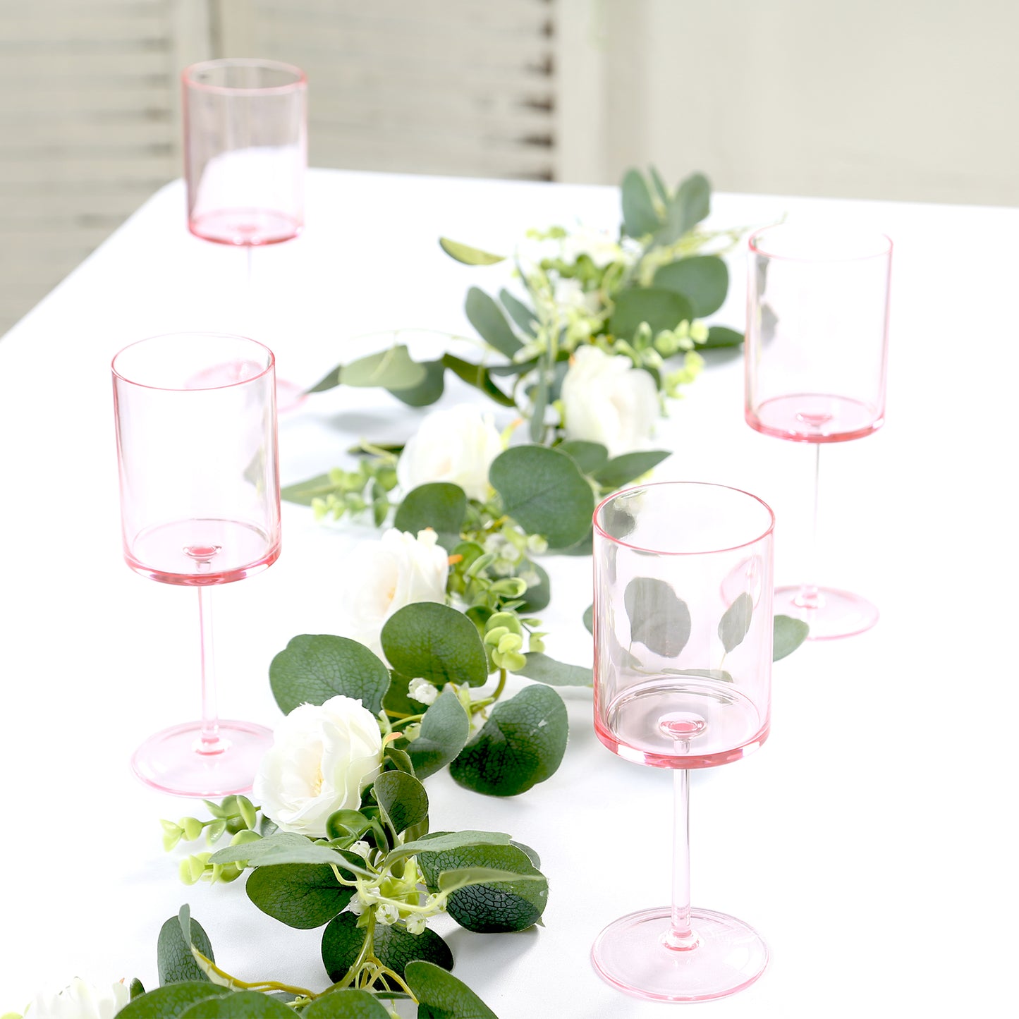 Transparent pink reusable cocktail glasses with long stems on a table.