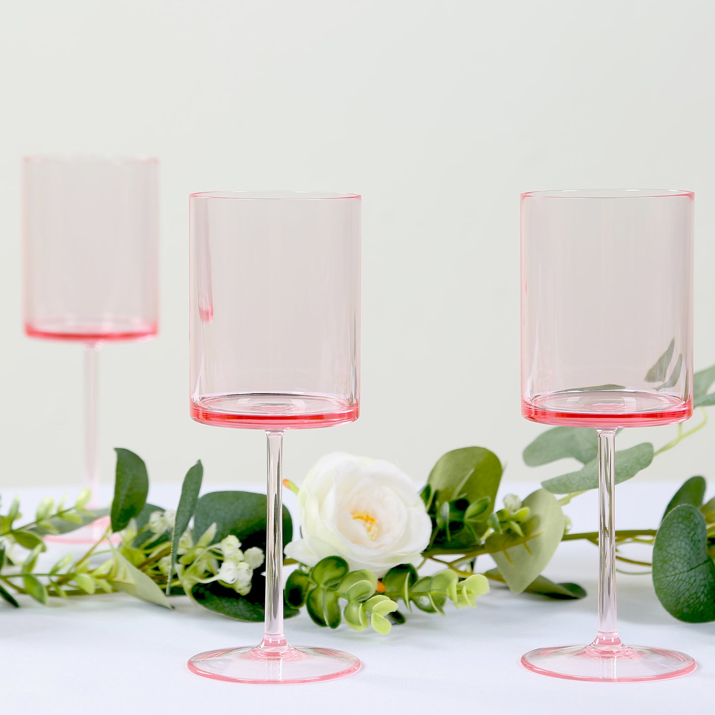 Transparent blush plastic reusable cocktail glasses with long stems.